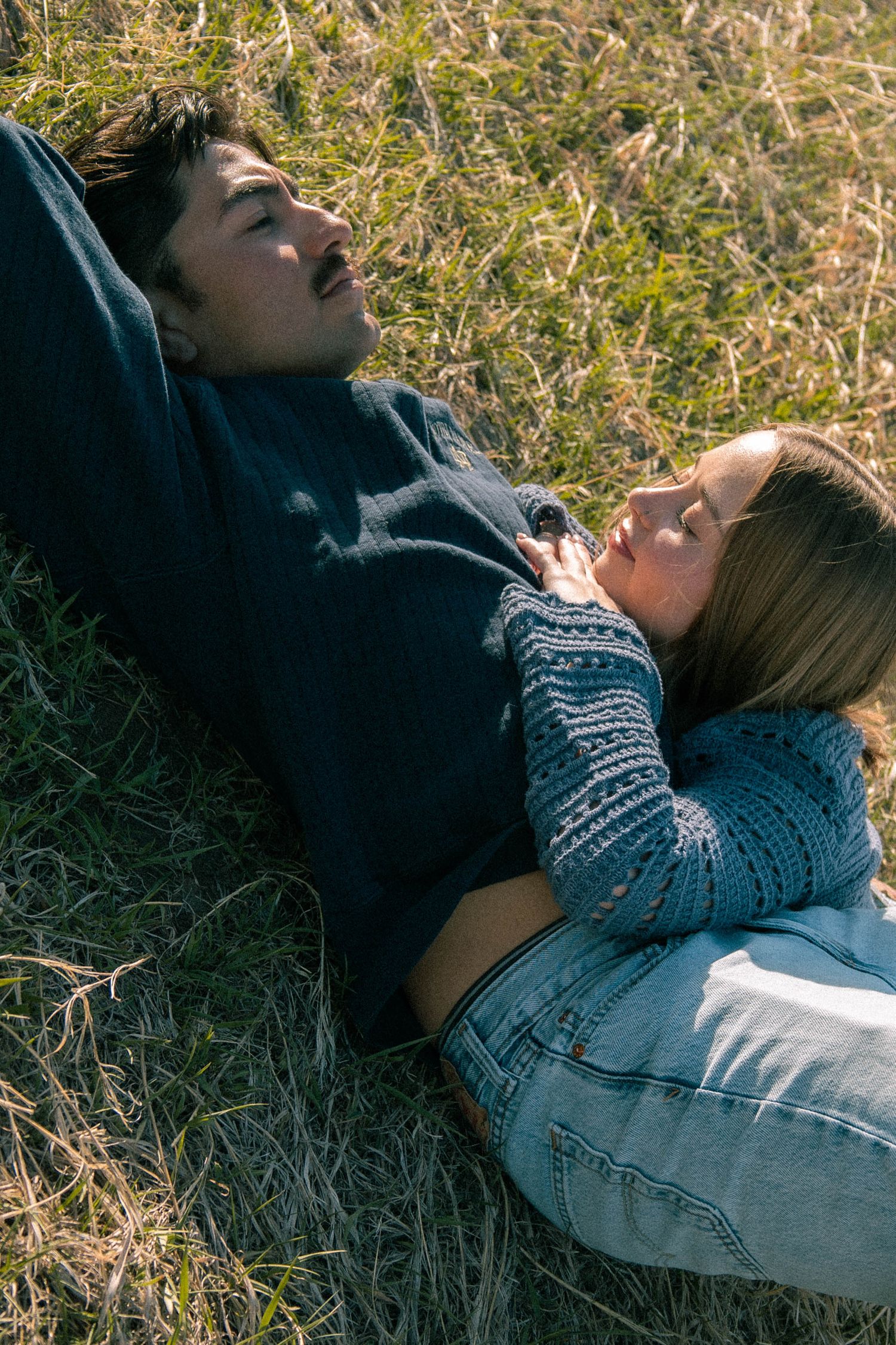 A couple lying on the grass with the woman lying on the man's stomach in a green field in Boulder, Colorado