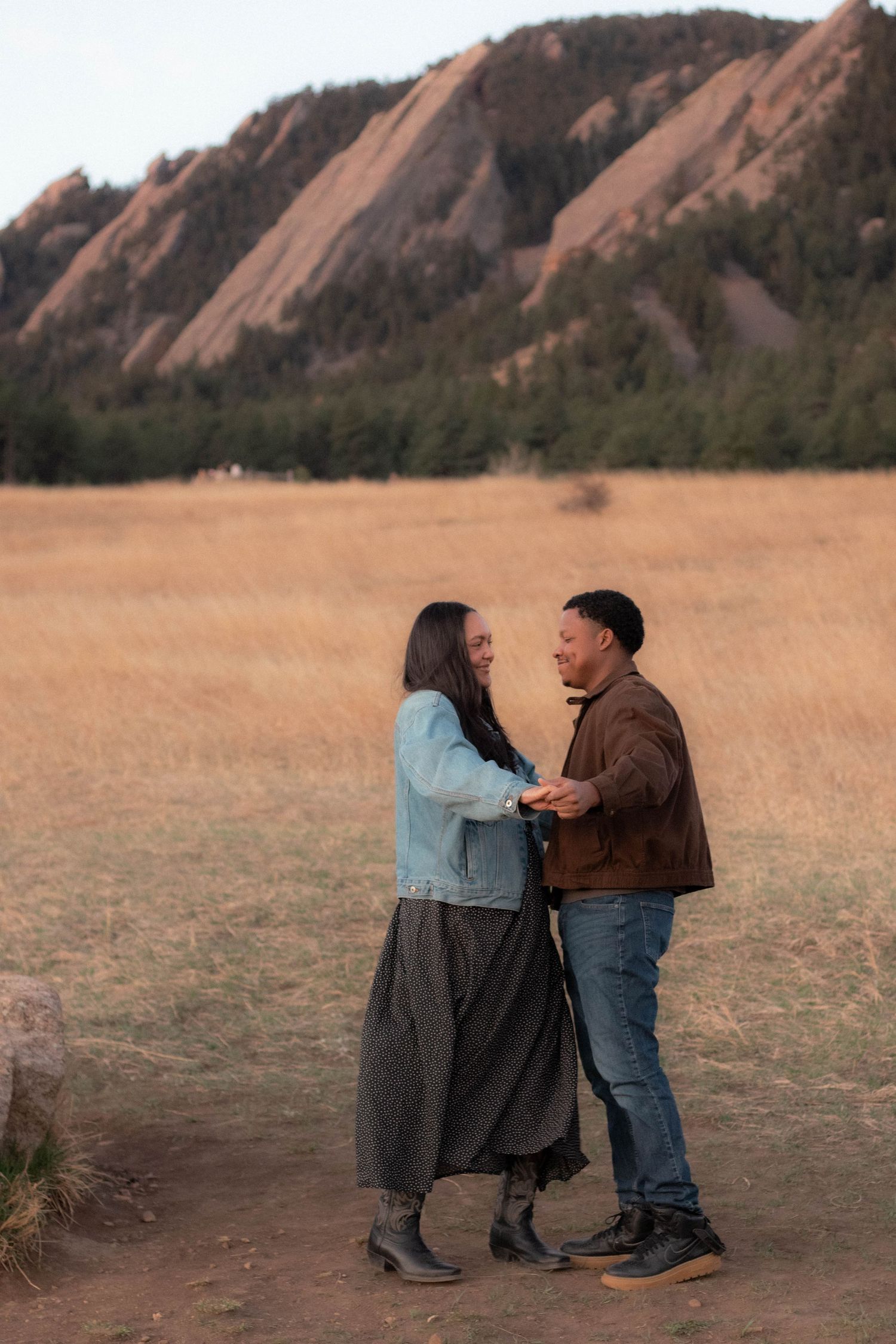A couple holding hands and swaying in front of the flatirons in Boulder, Colorado