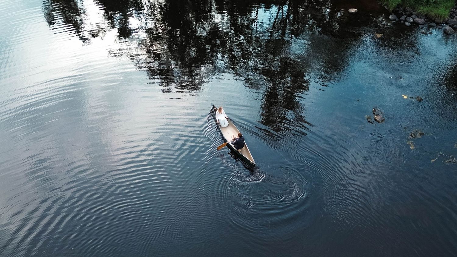Aerial drone view of a lone person paddling a small boat on a reflective calm lake.