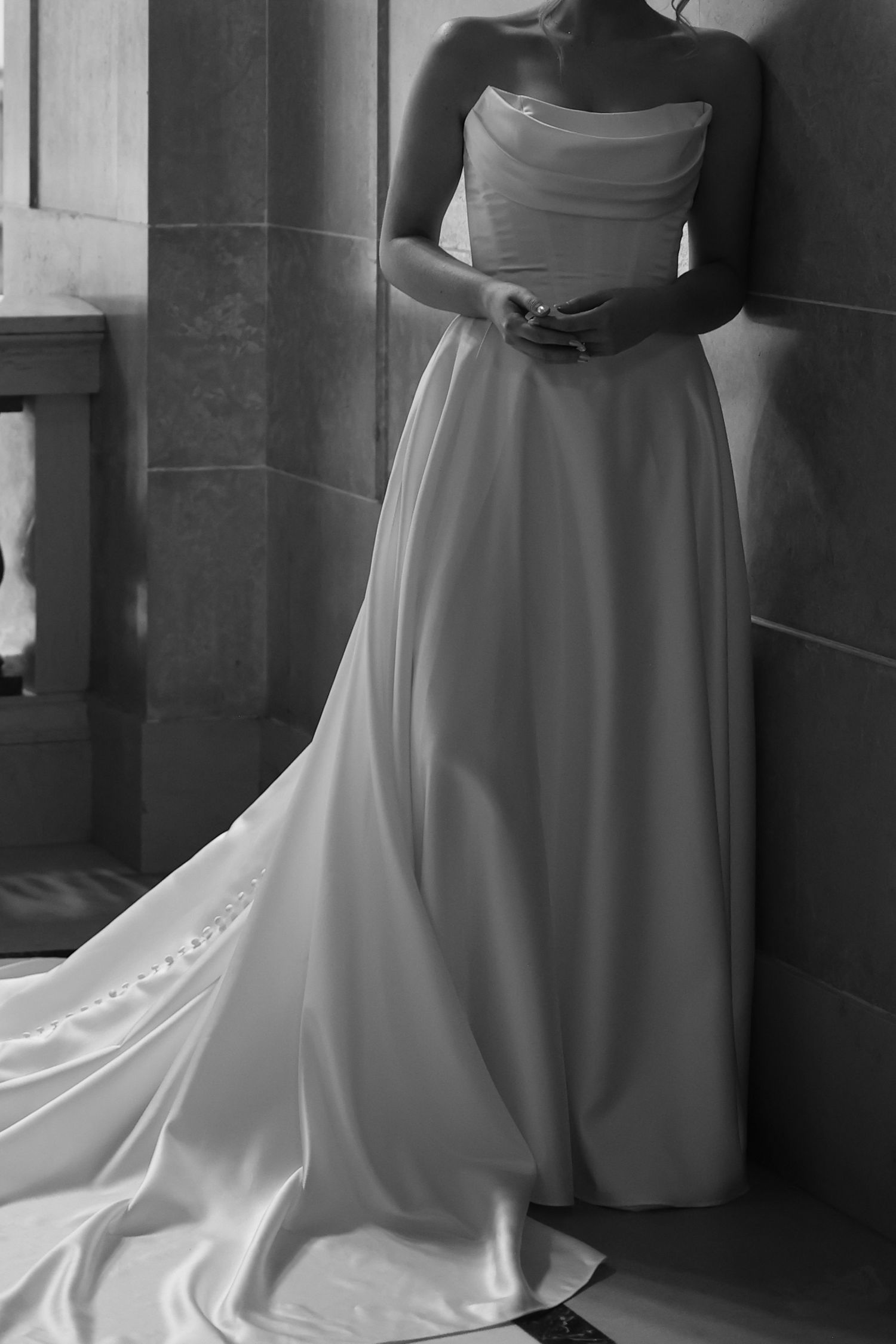 Elegant bride in a strapless satin wedding gown with a long train posing in black and white.
