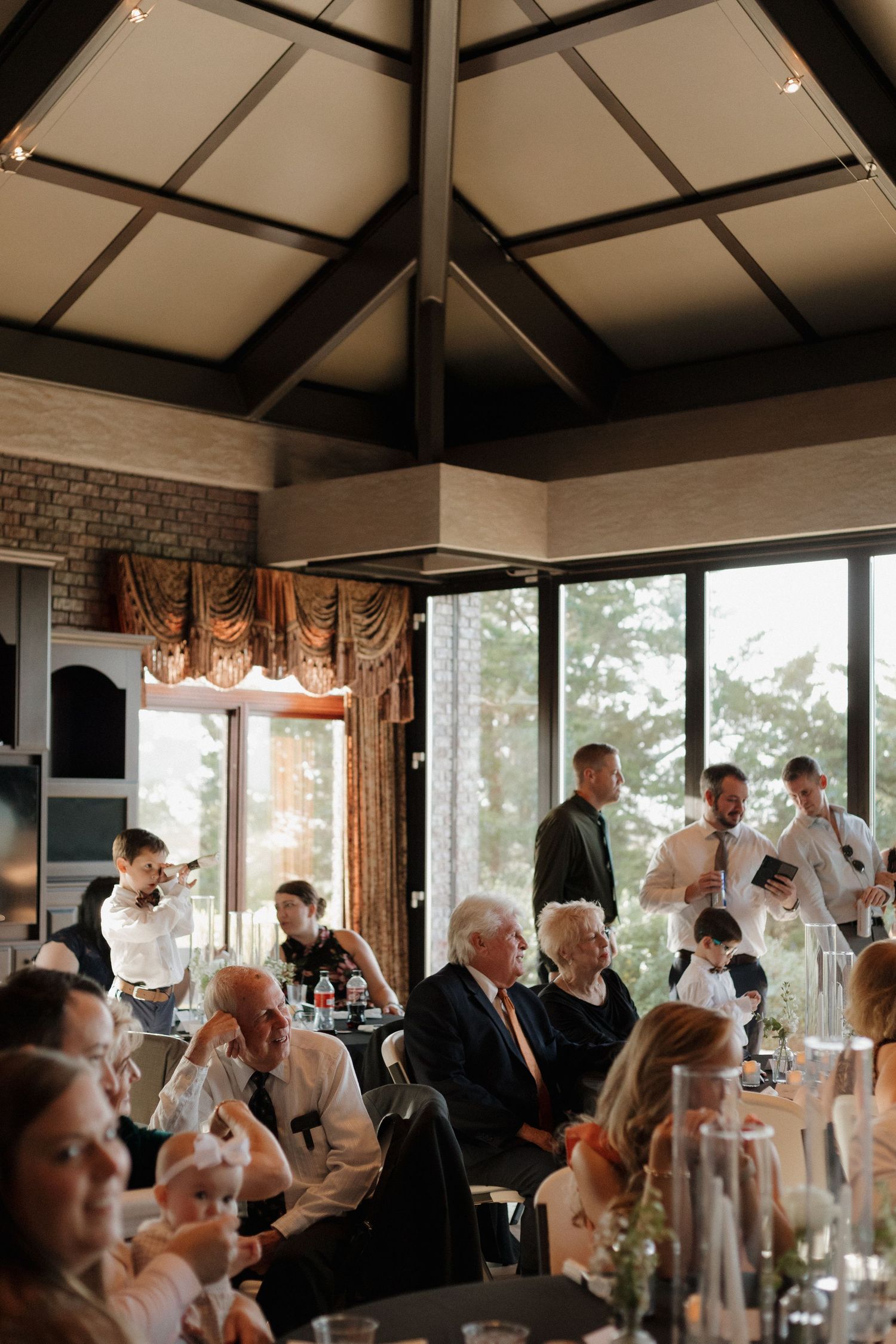 Wedding reception venue with large windows and guests seated at decorated tables.