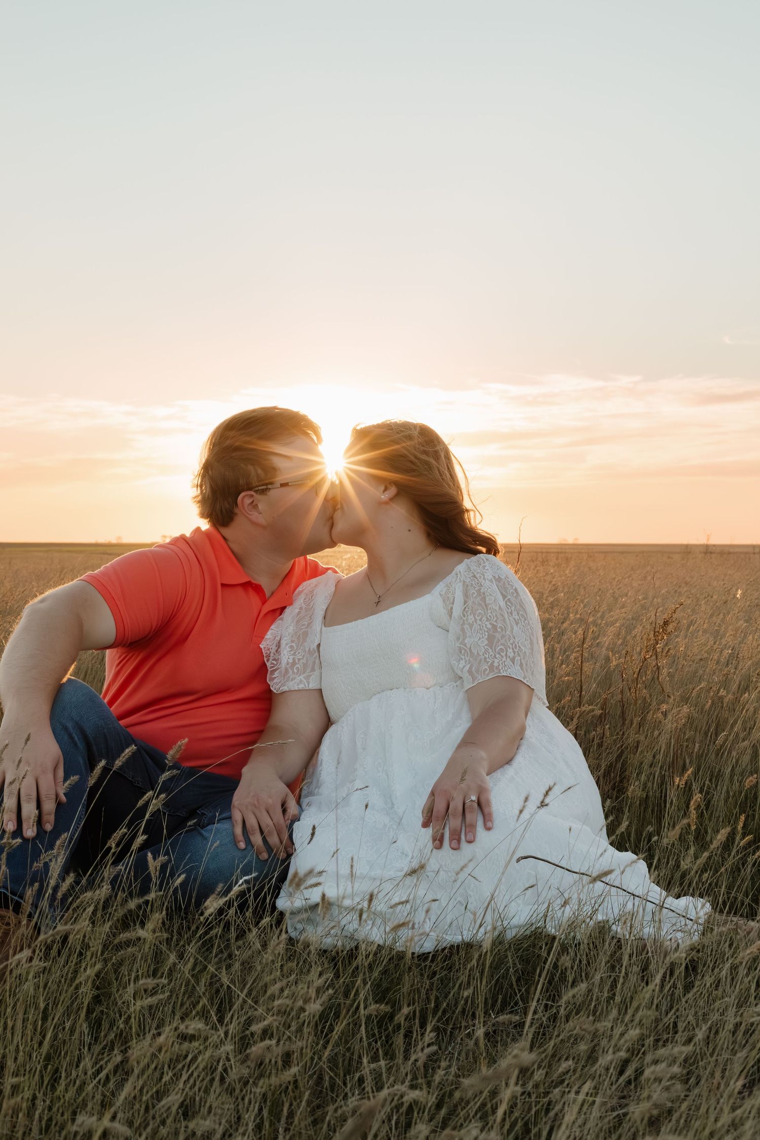A couple reclines in tall grass during a dreamy sunset photoshoot.