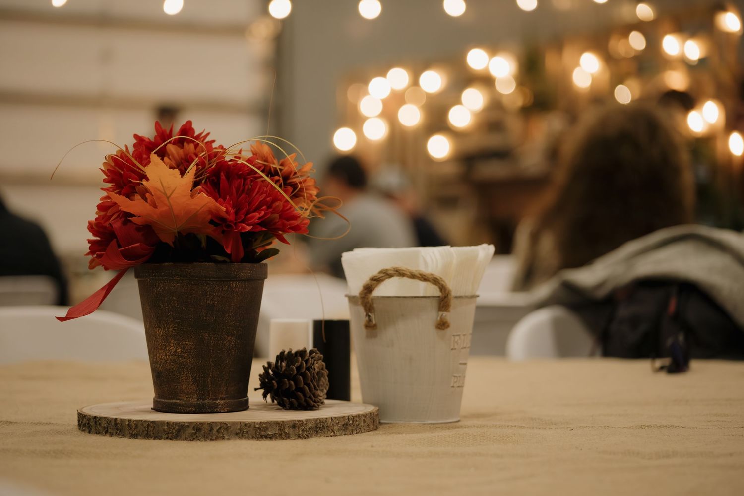 Decorative fall centerpieces with red flowers and pinecones on wooden slices.