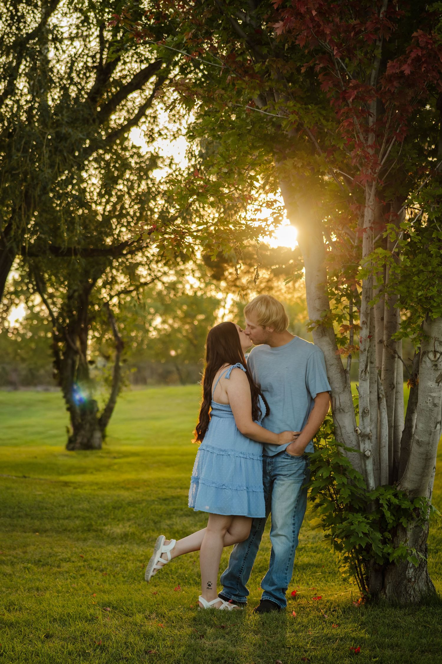 A couple walks hand in hand through a sunlit park with golden light filtering through the trees.