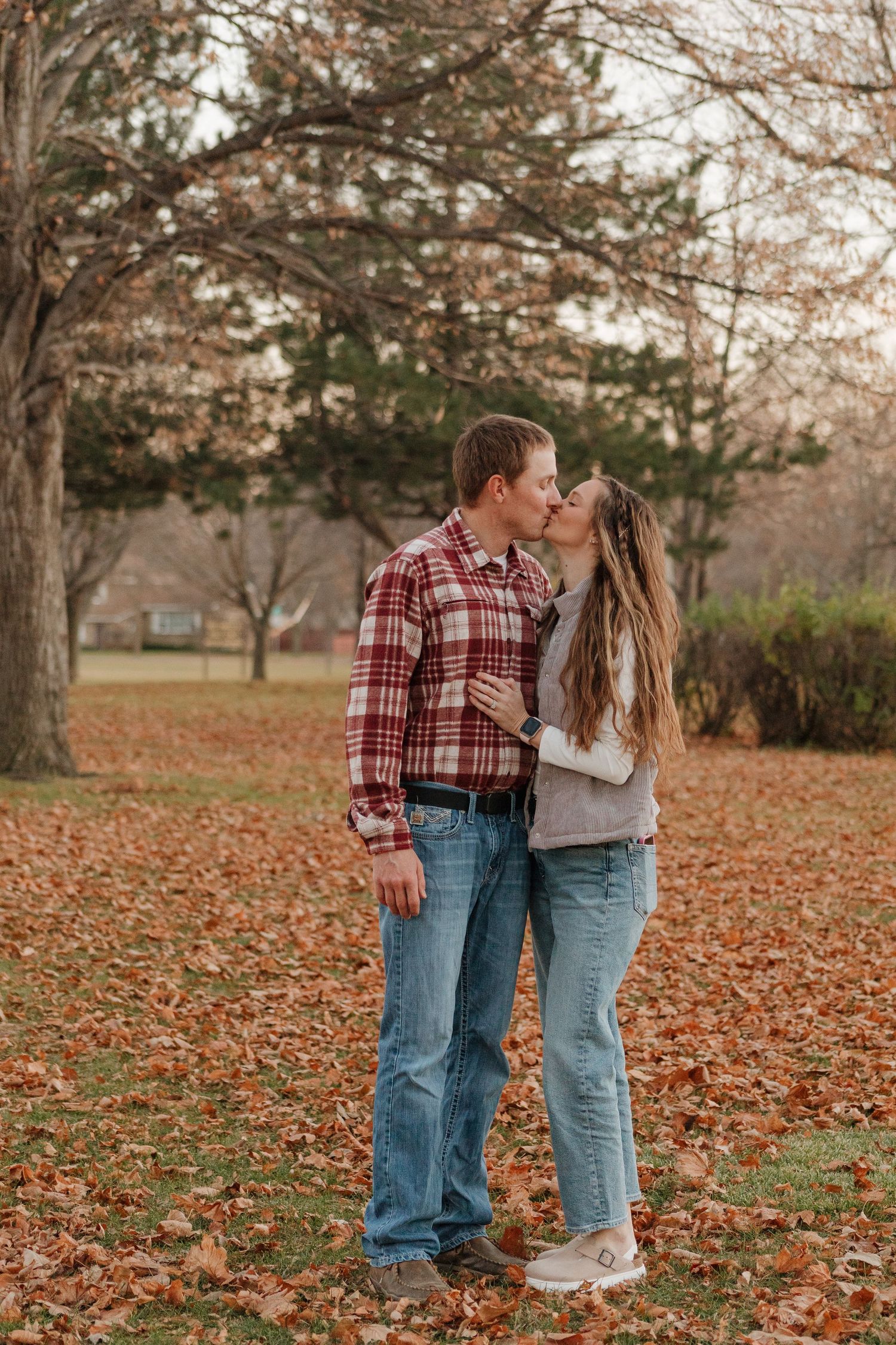 Romantic couple in casual wear walking through fallen autumn leaves.