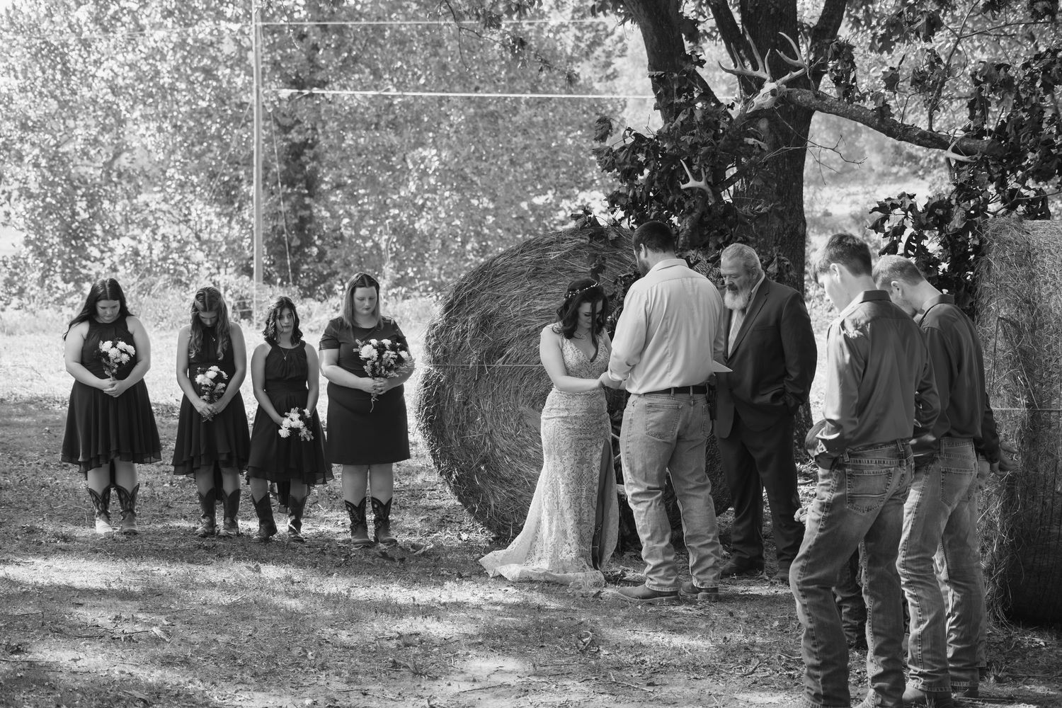 A wedding party stands together outdoors for group photos on a sunny day.