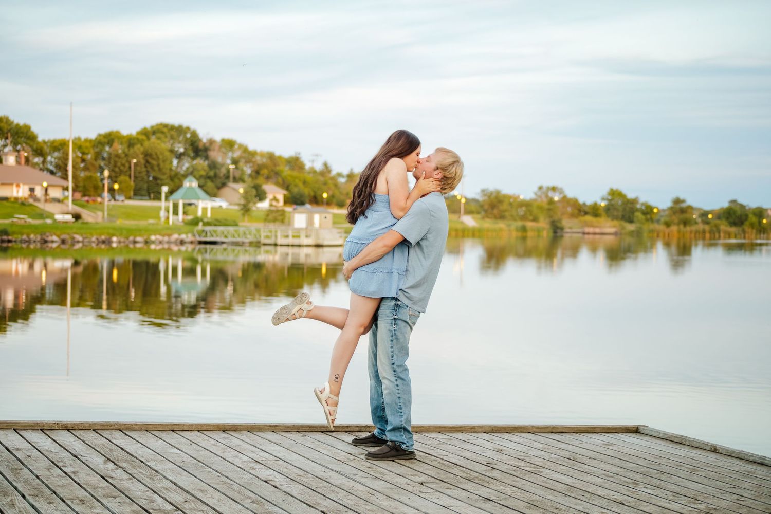 A playful couple poses on a wooden dock overlooking a serene lake.