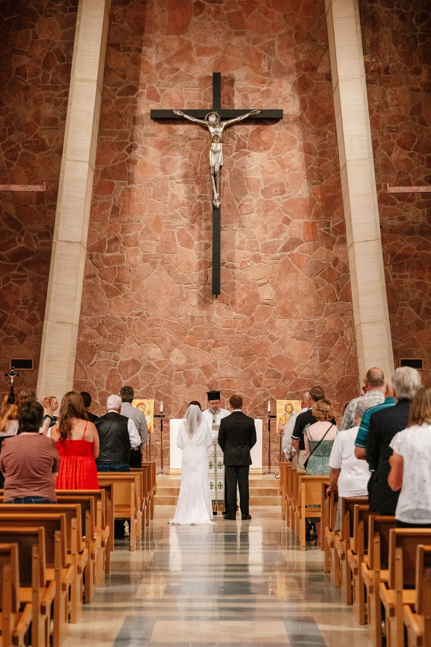 Church interior with wooden pews and stone walls showing a wedding ceremony in progress.
