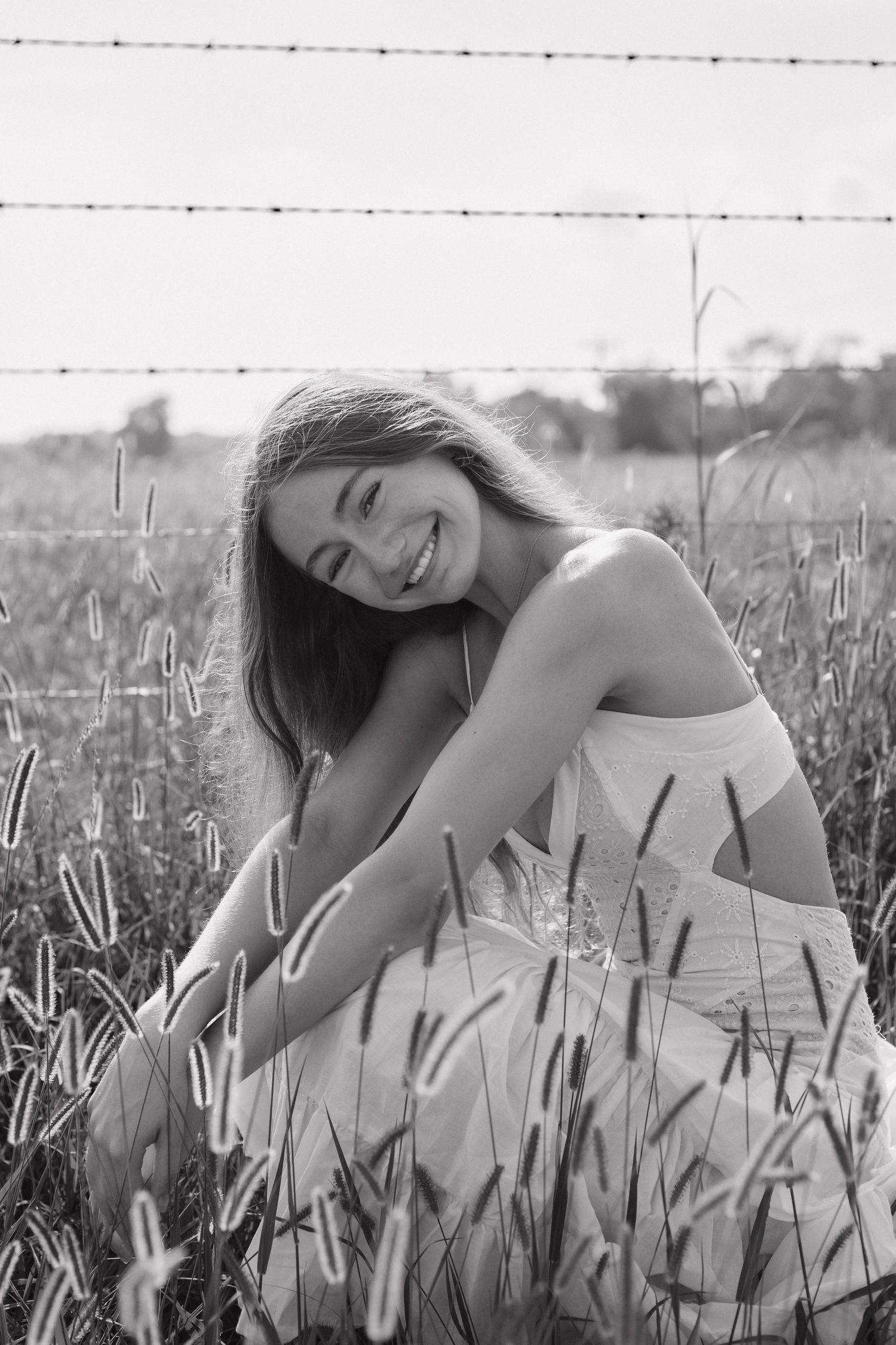 A joyful portrait in a summer field with tall grass and barbed wire fence in black and white.