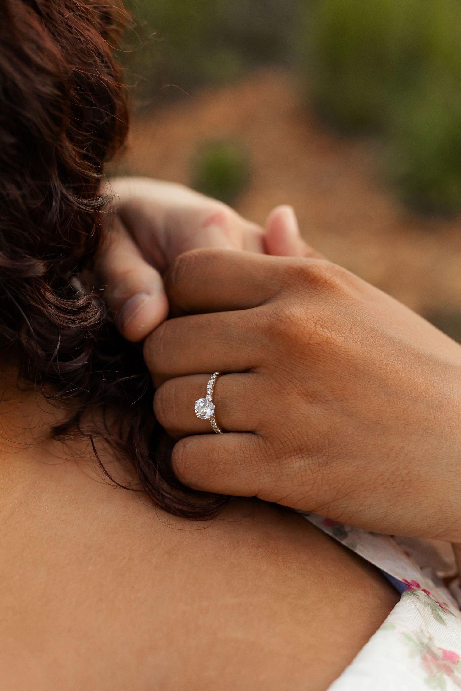 Close-up of a sparkling diamond engagement ring on a hand against a dark background.
