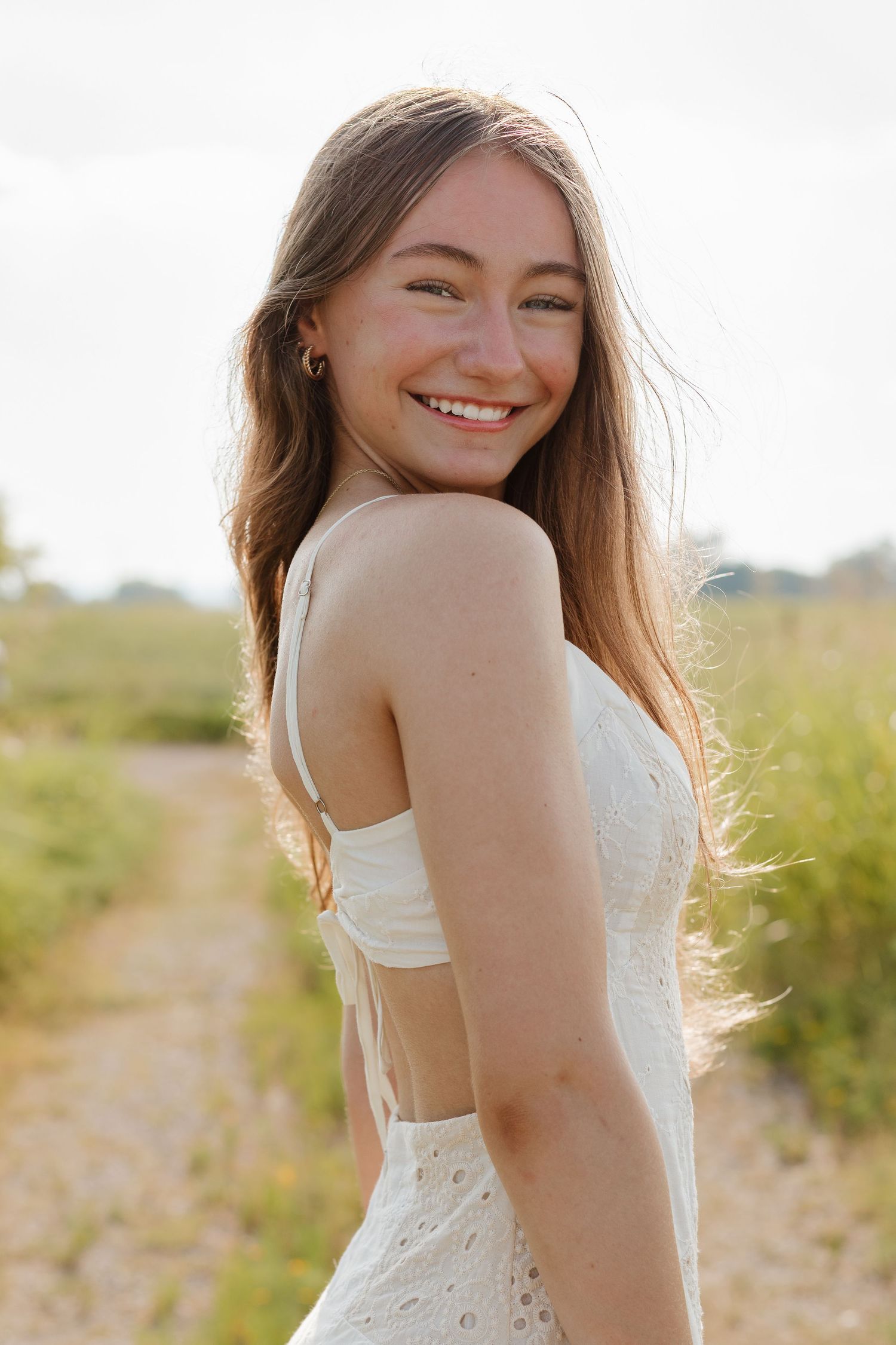 A sunlit outdoor portrait showcasing a white summer dress in a natural field setting.