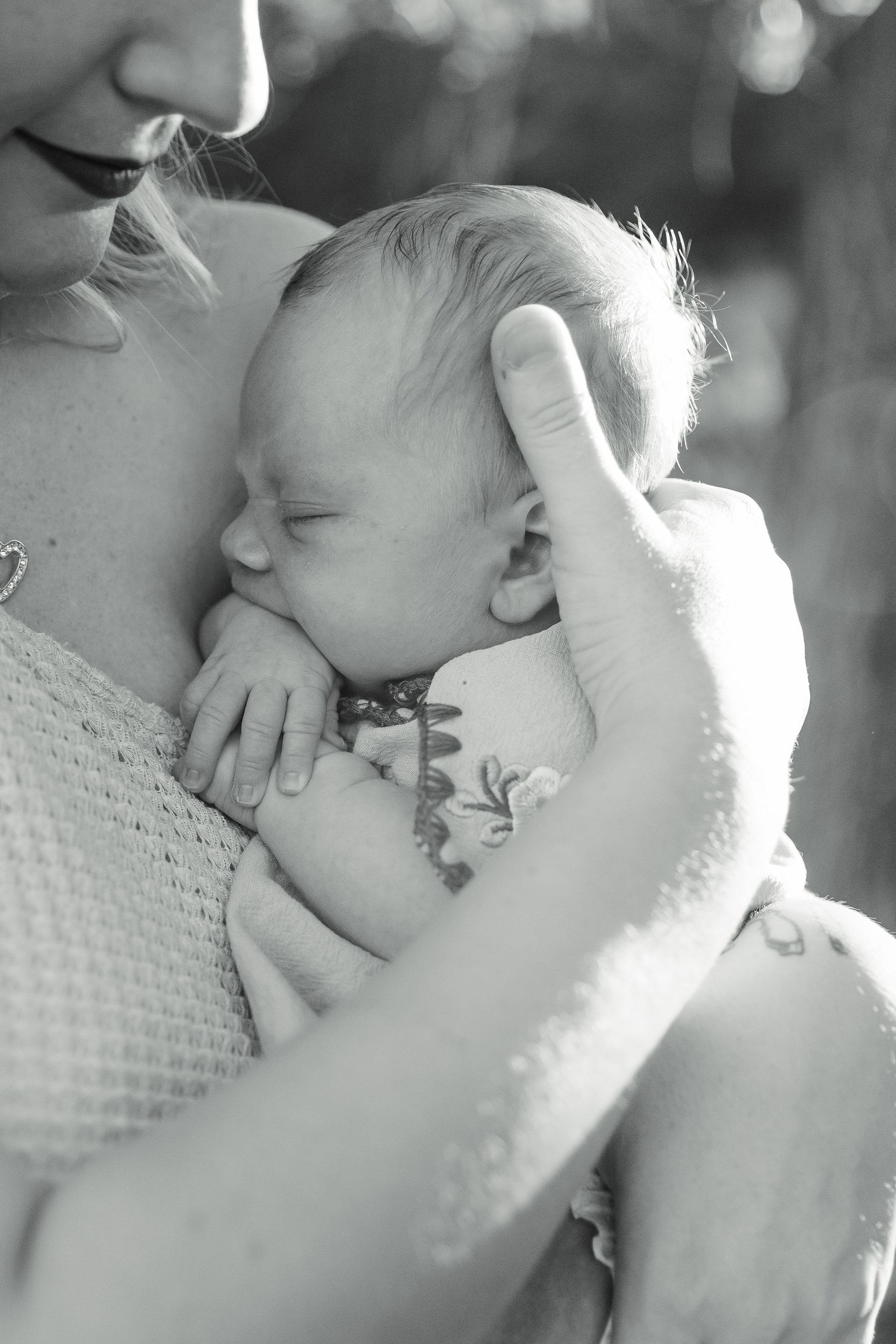 A tender black and white portrait of a sleeping newborn baby being cradled against someone's chest.