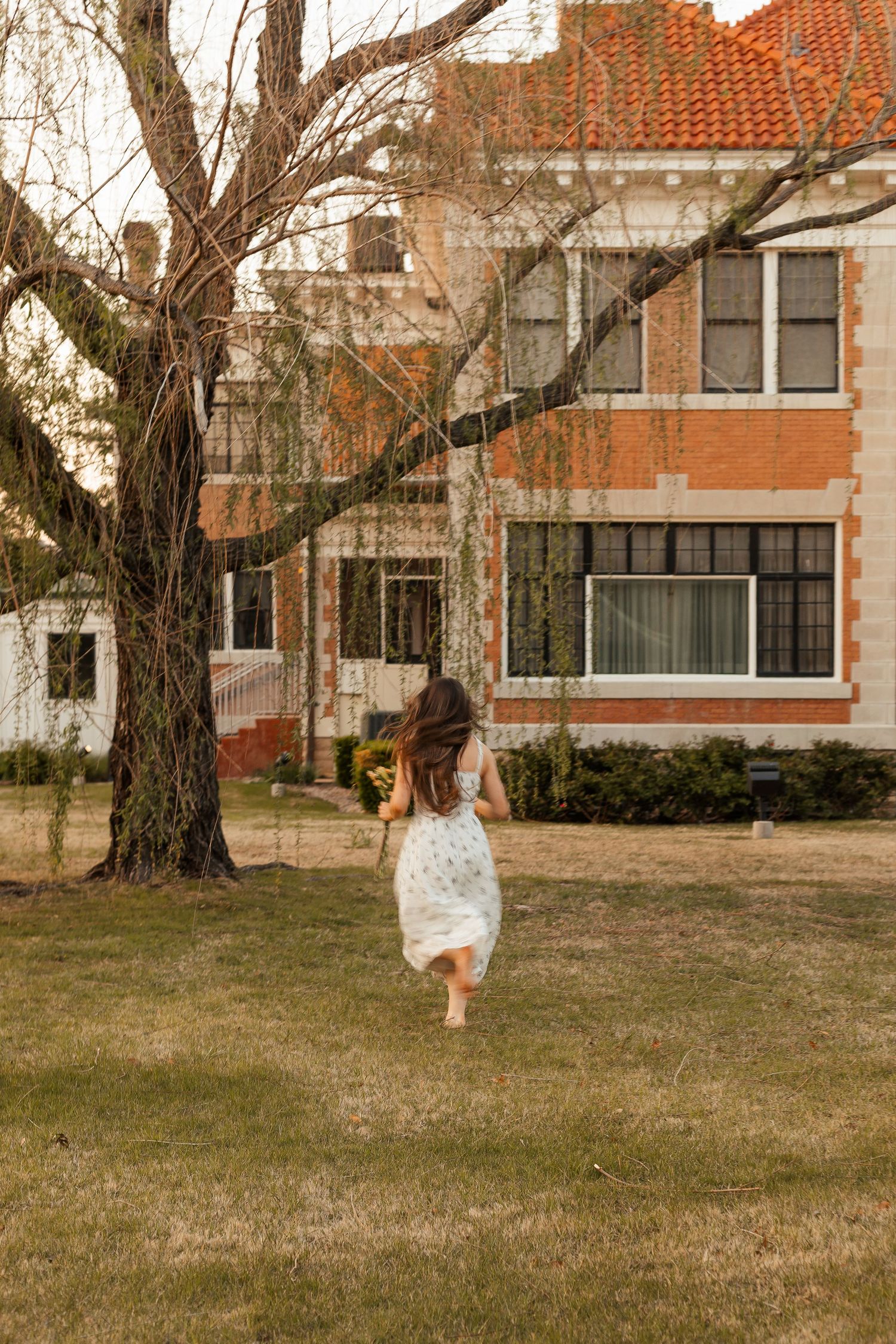 Person in white dress runs under a willow in warm sunset lighting in Bartlesville, Oklahoma.