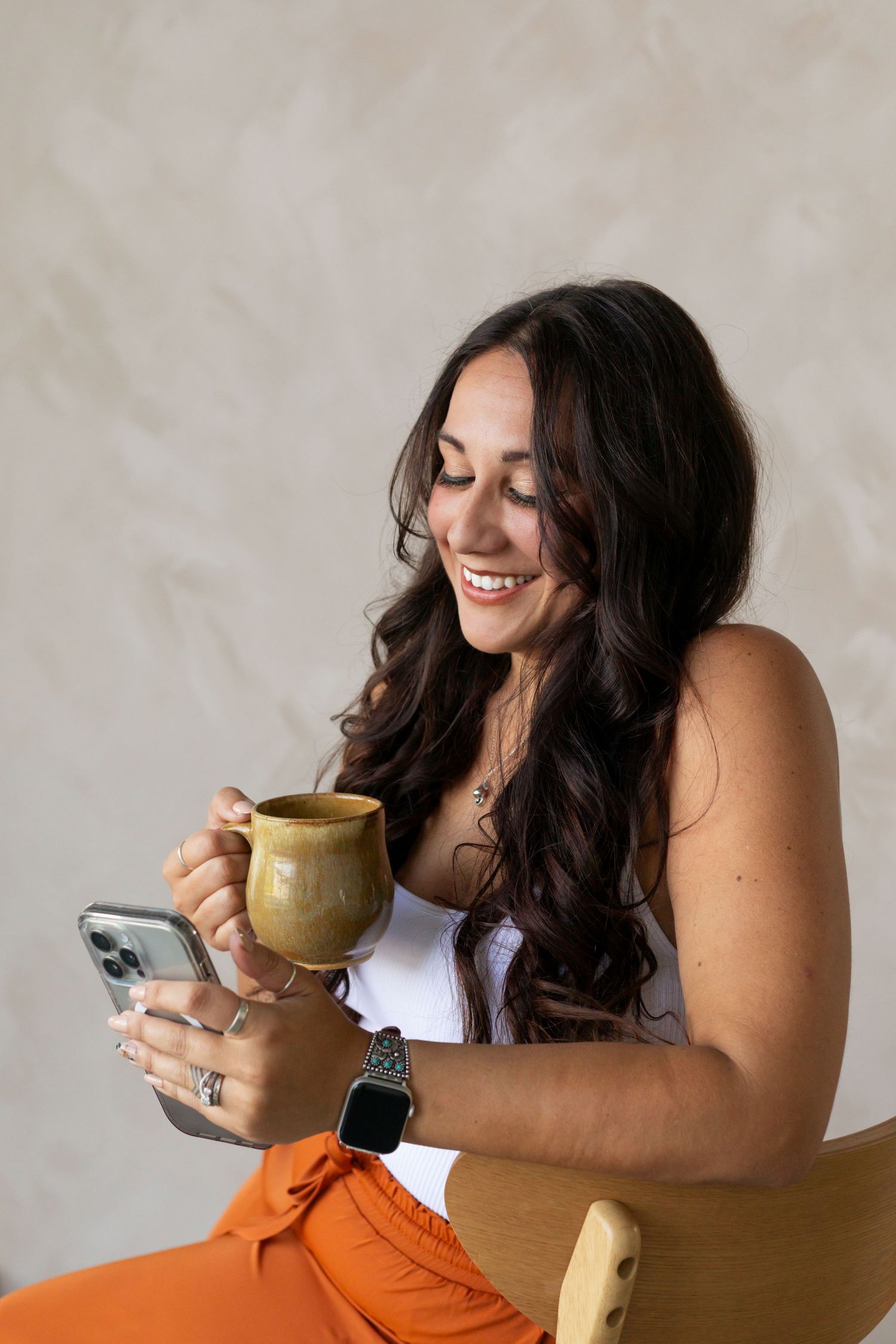 Casual lifestyle photos enjoying coffee and phone in orange pants and white top.
