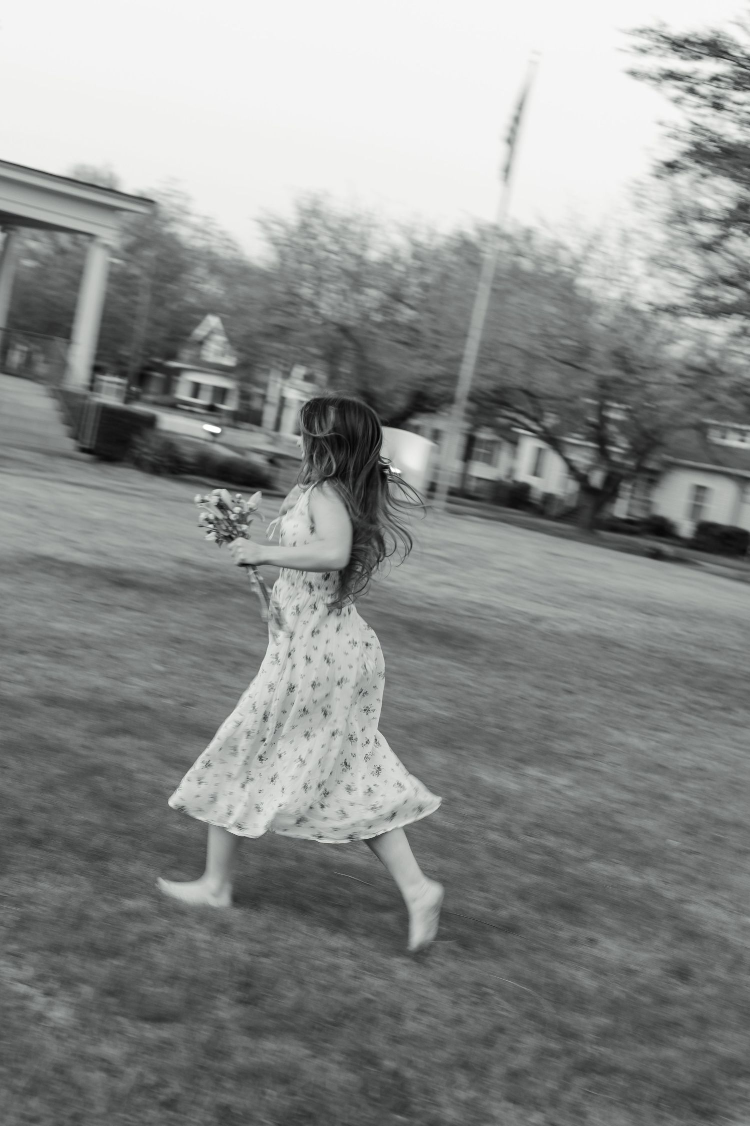 Woman in white dress runs playfully across grass field in black and white motion shot in Bartlesville, Oklahoma.