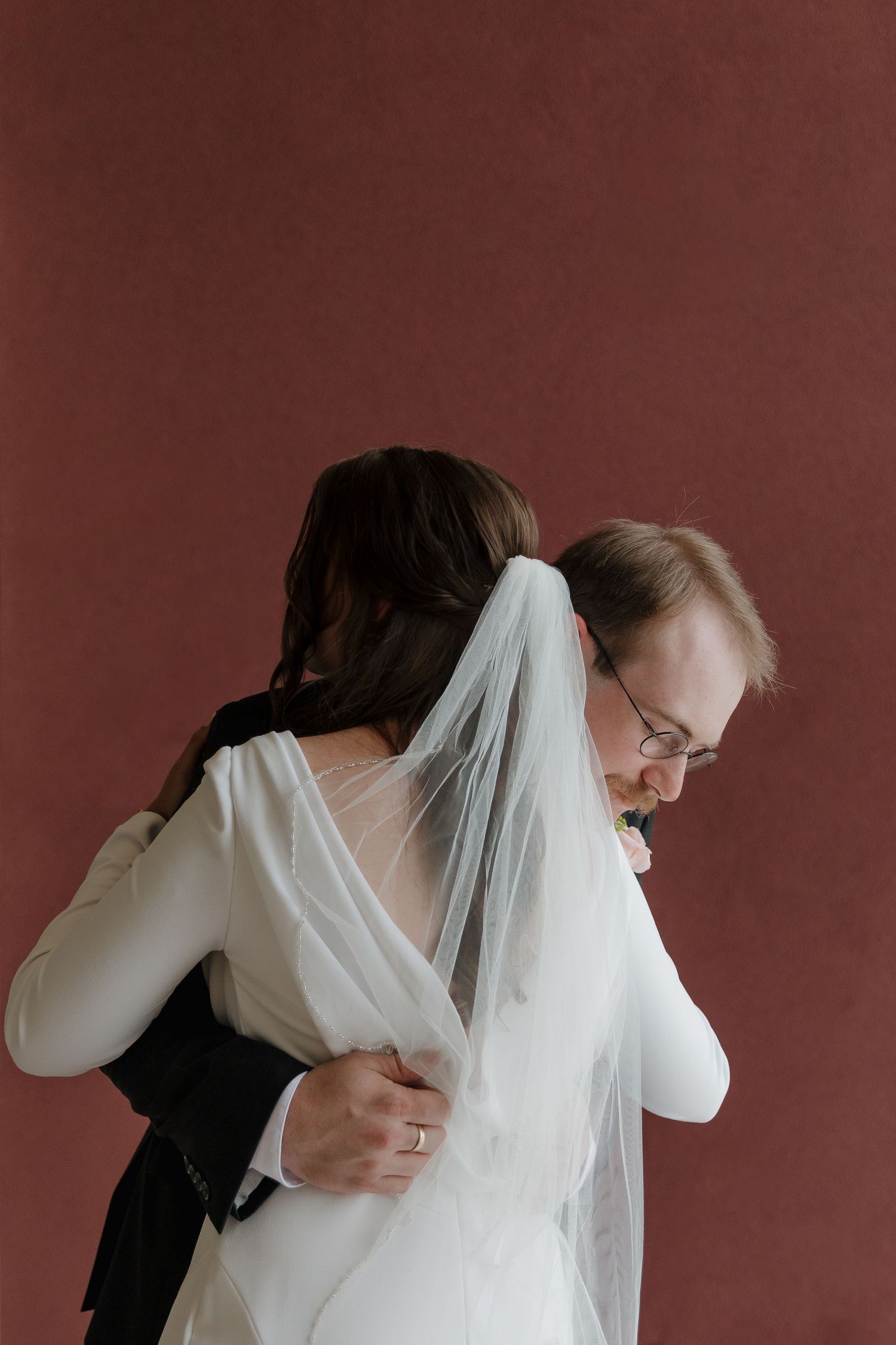 An intimate wedding moment against a burgundy backdrop in a Catholic church located in Rapid City, South Dakota.