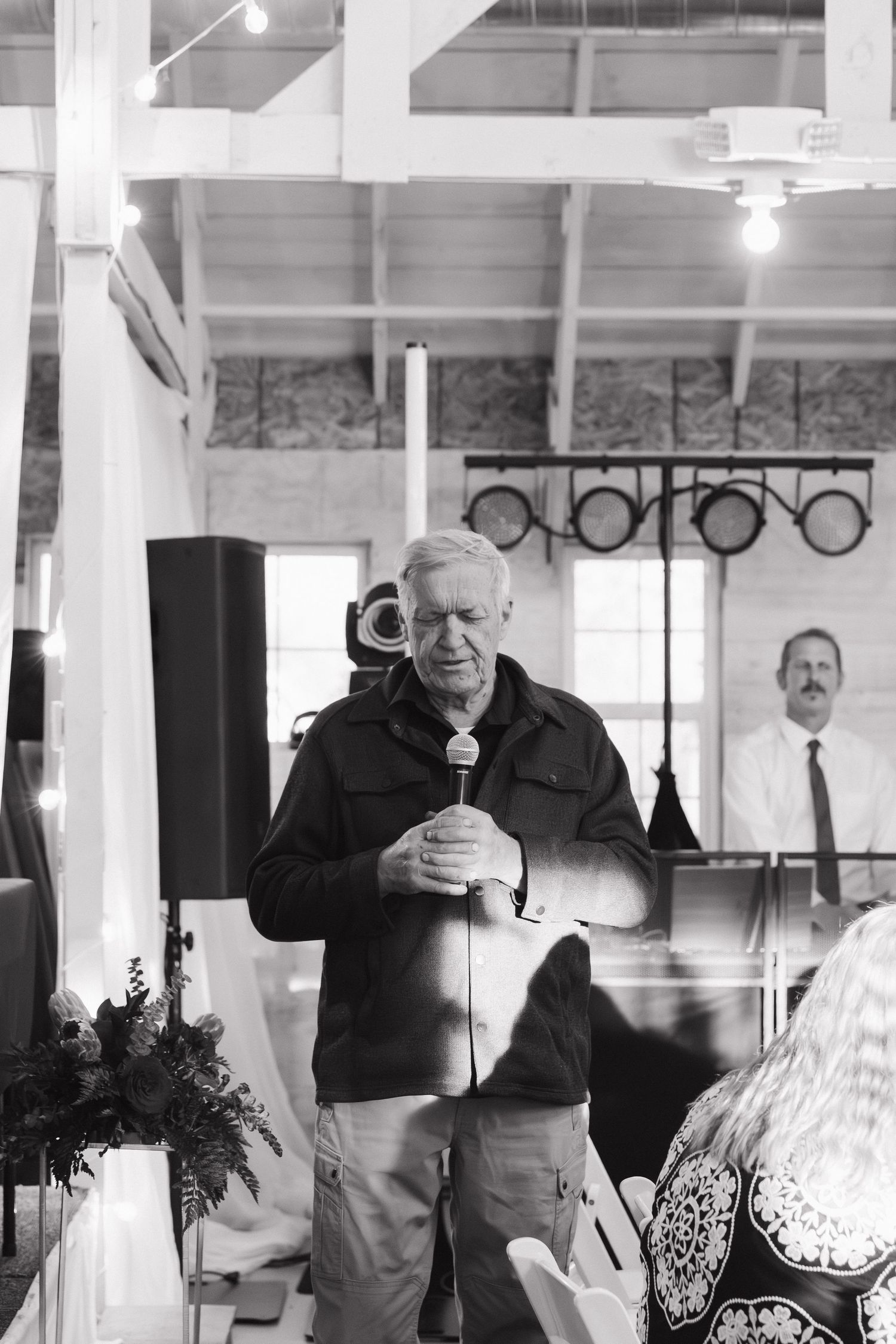 Black and white photo of wedding reception with guests mingling in bright indoor venue.
