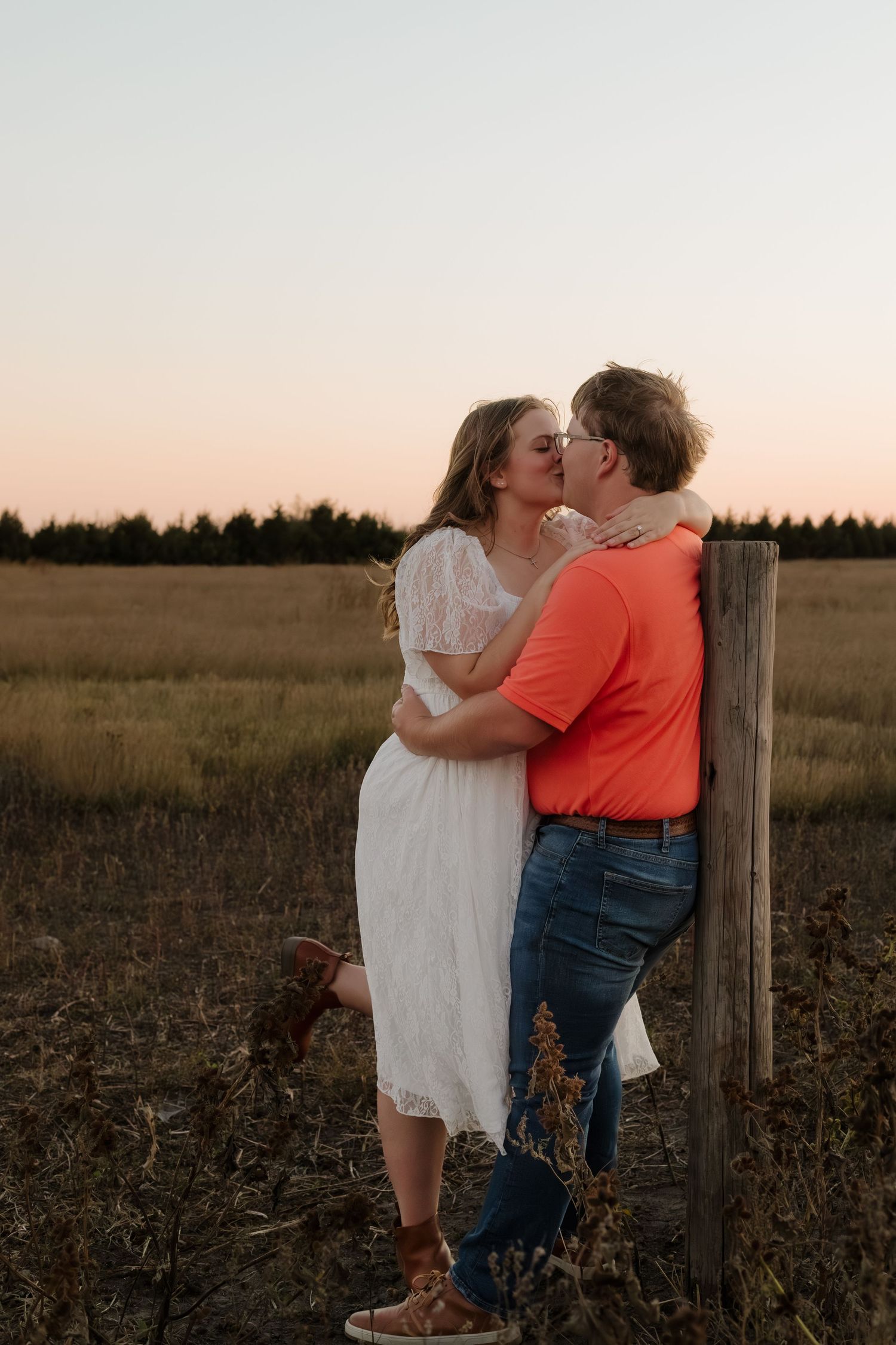 A romantic sunset portrait session in a rustic field with a wooden fence post.