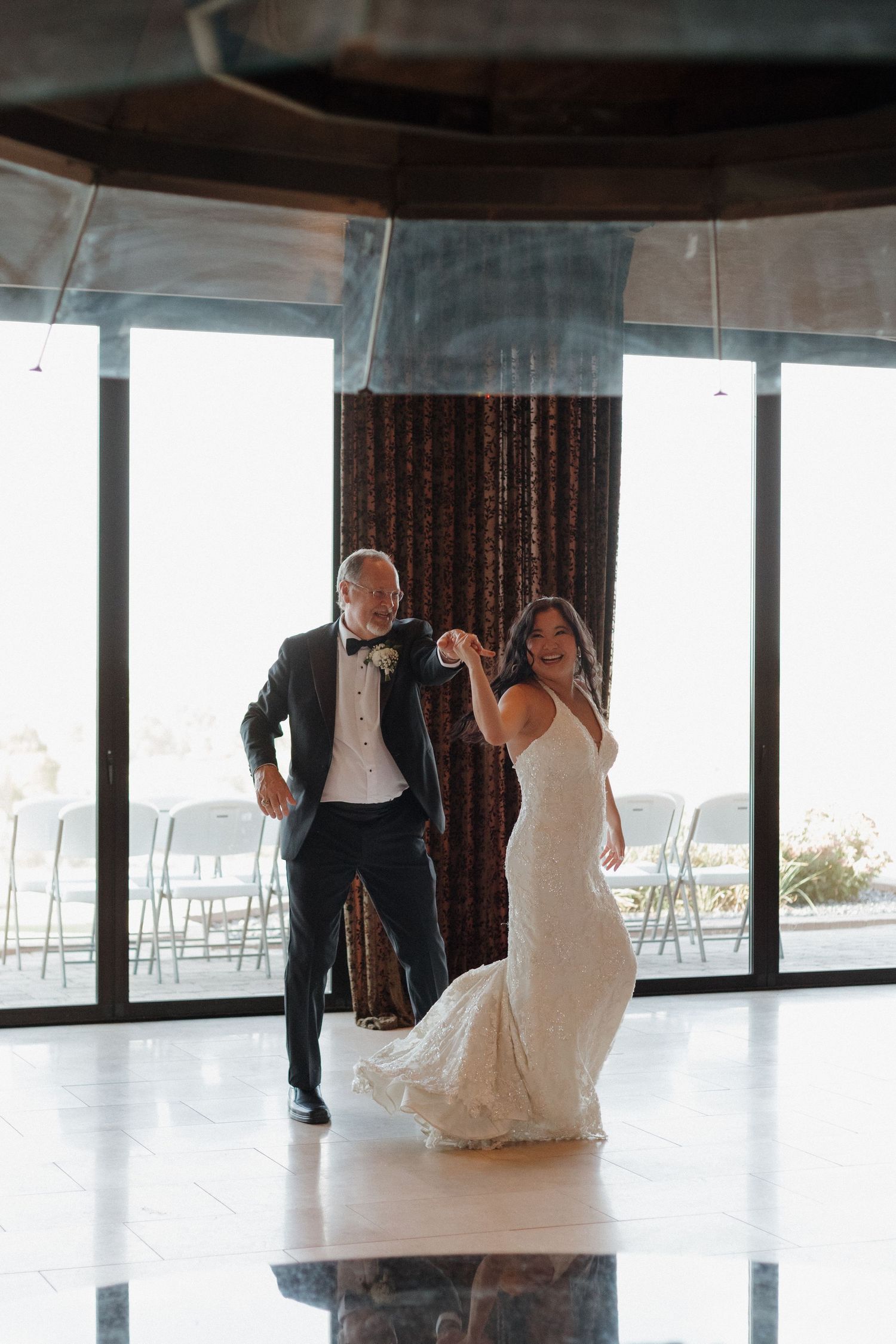 Wedding couple dancing in spacious venue with large windows.