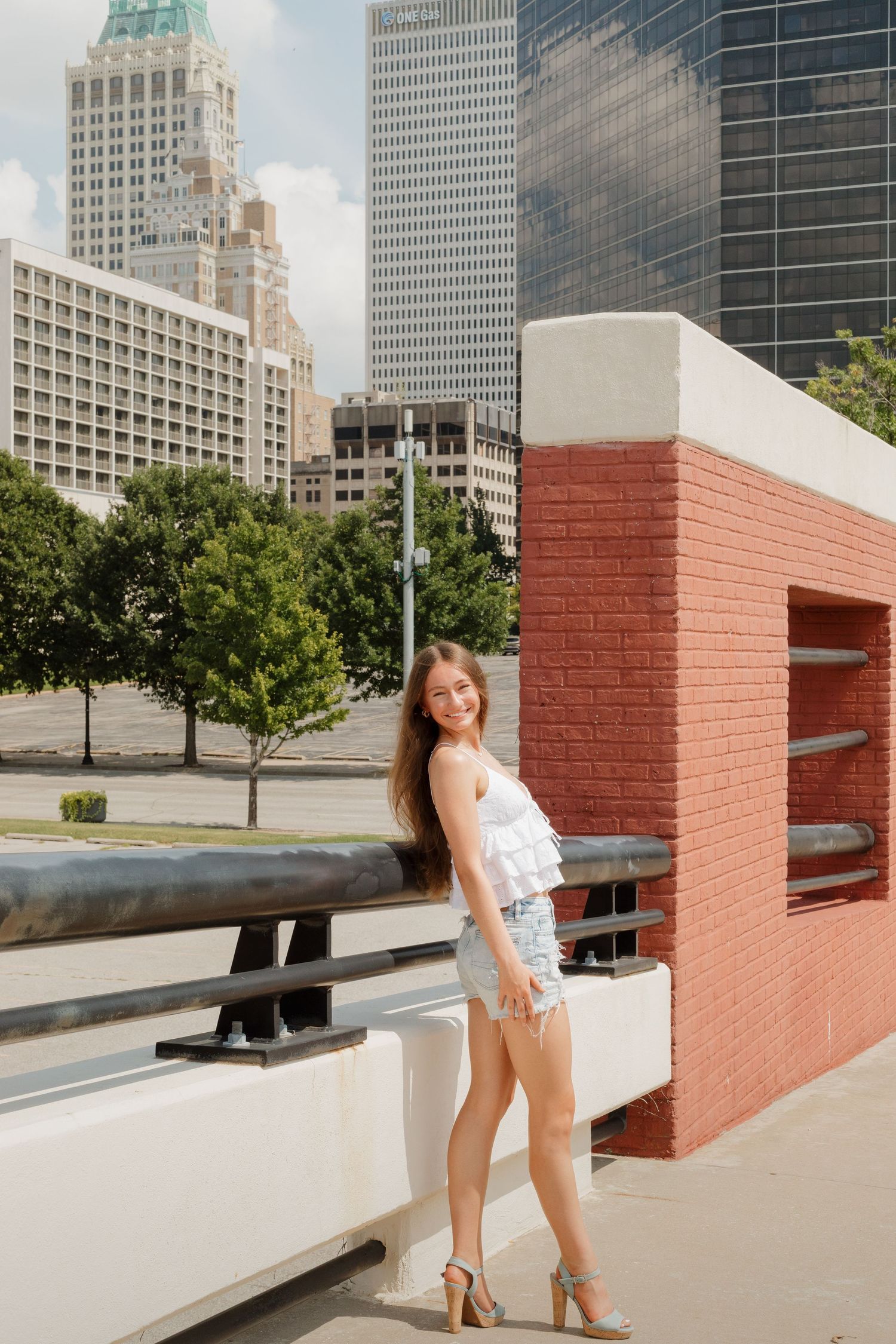 Urban fashion portrait with city skyline and red brick wall in background.