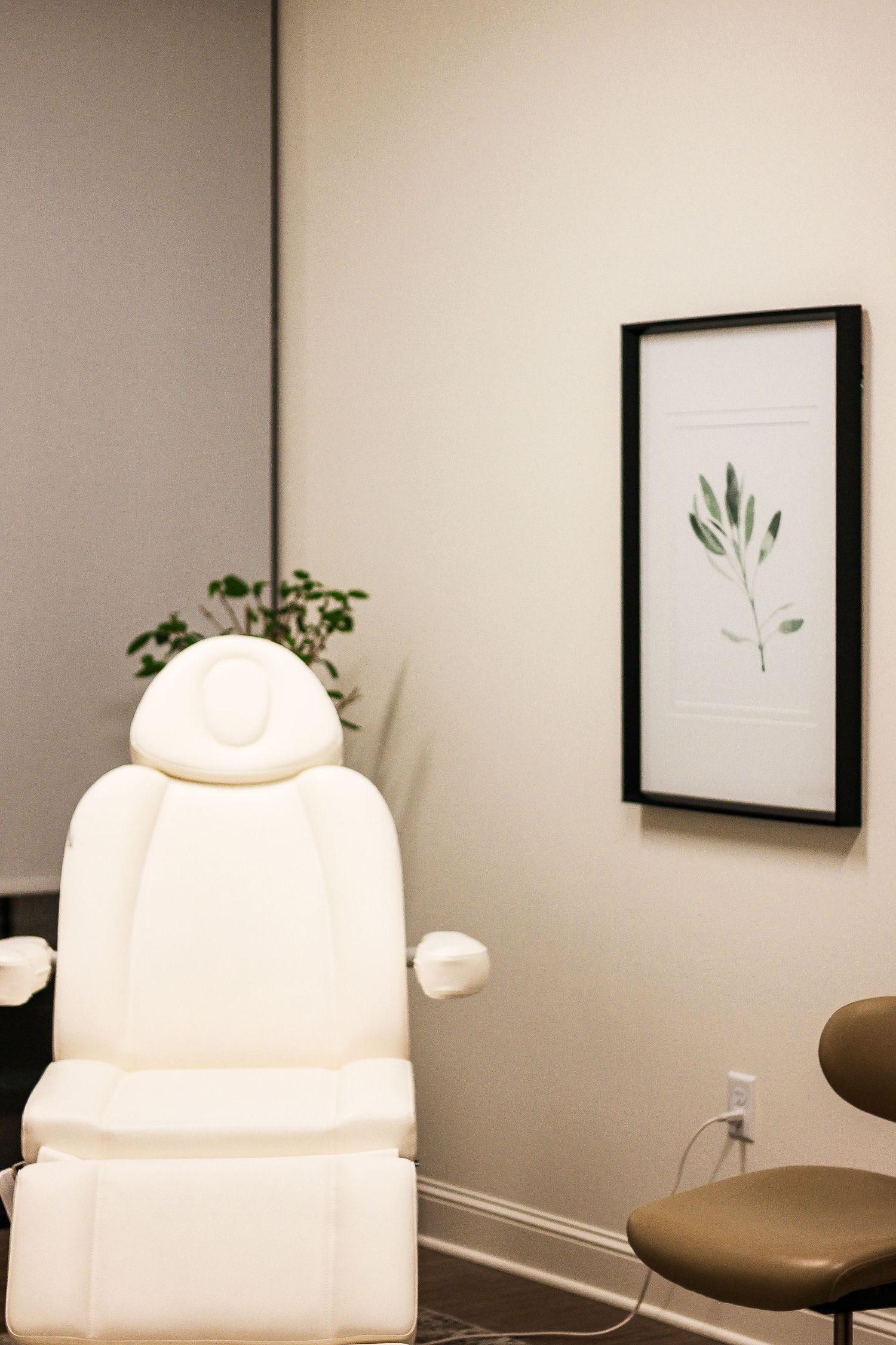 Clean spa treatment room with white chairs and minimalist botanical artwork on grey walls.