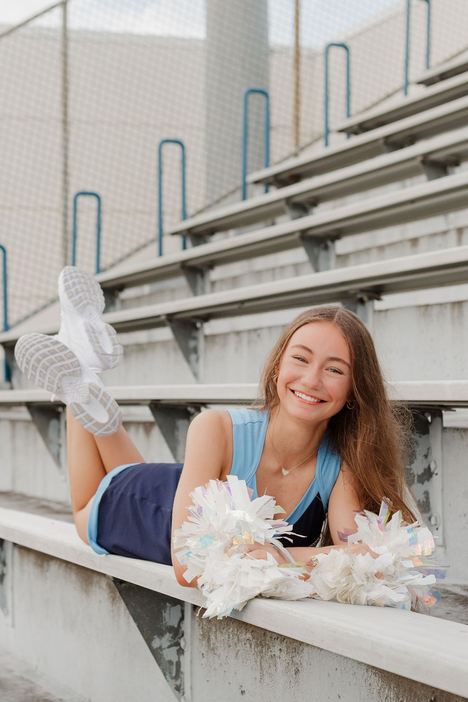 Cheerleader lying on concrete bleachers holding white and silver pom poms.