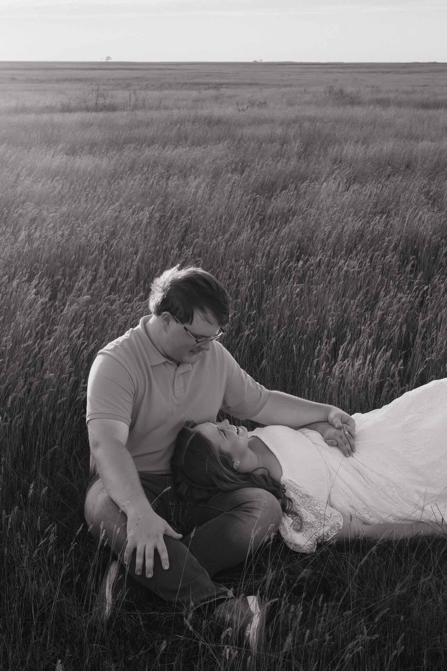 A black and white portrait of a couple sharing an intimate moment in a prairie field.