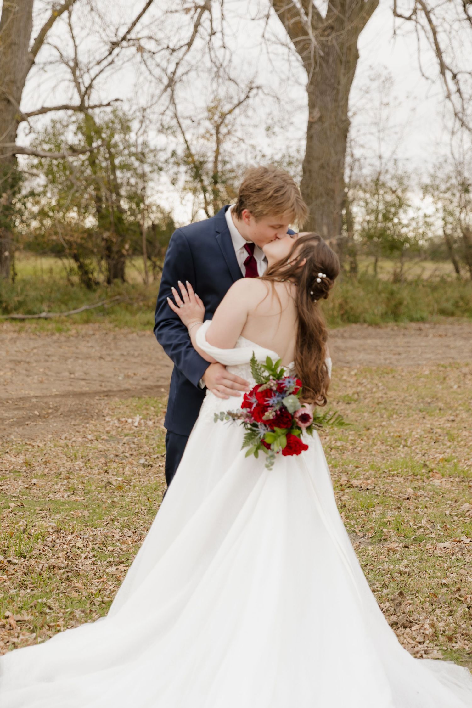 A romantic wedding couple shares a kiss while standing in a field with the bride wearing a flowing white gown.