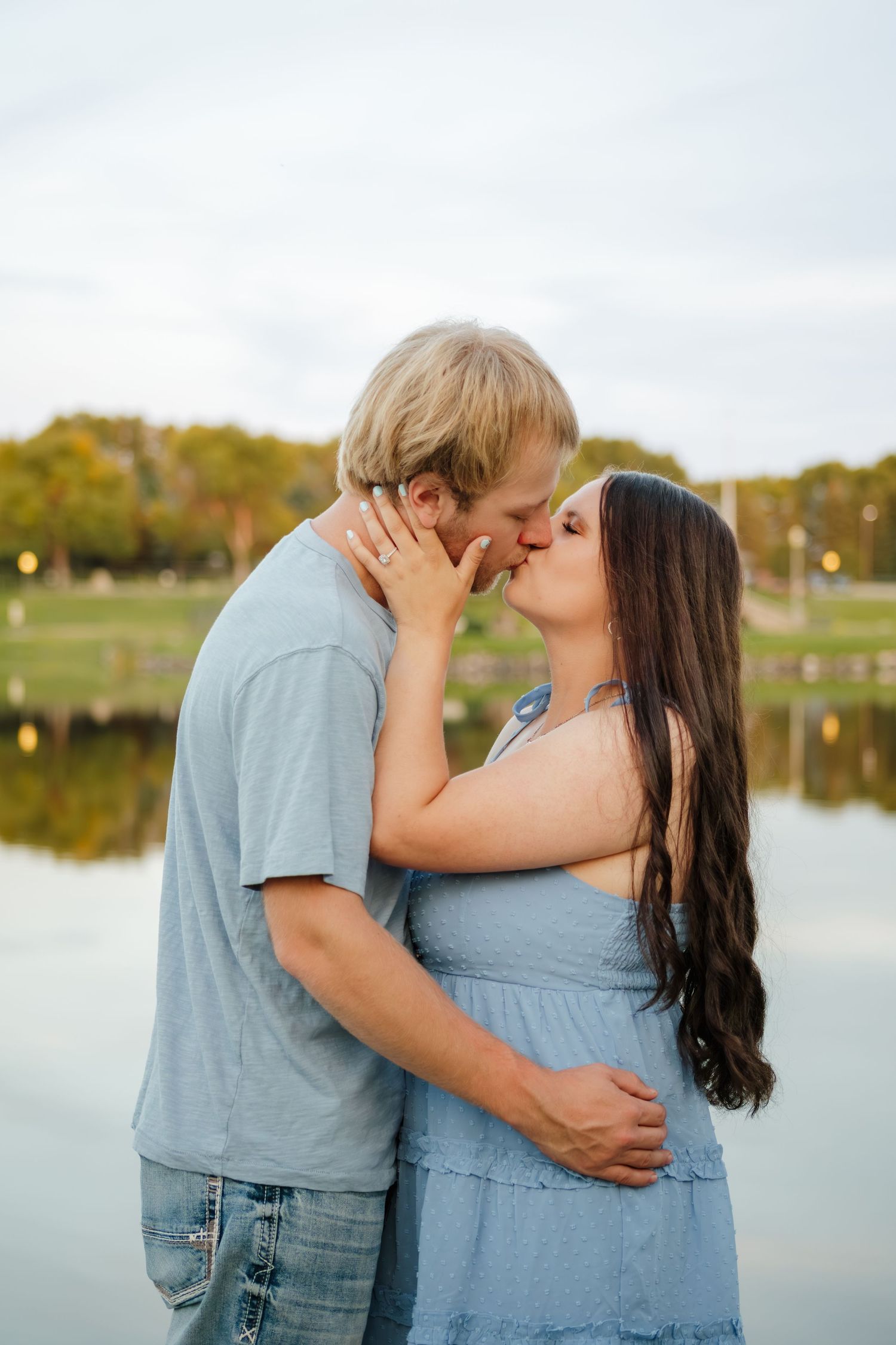 A tender moment captured by a lake with soft lighting and natural surroundings.