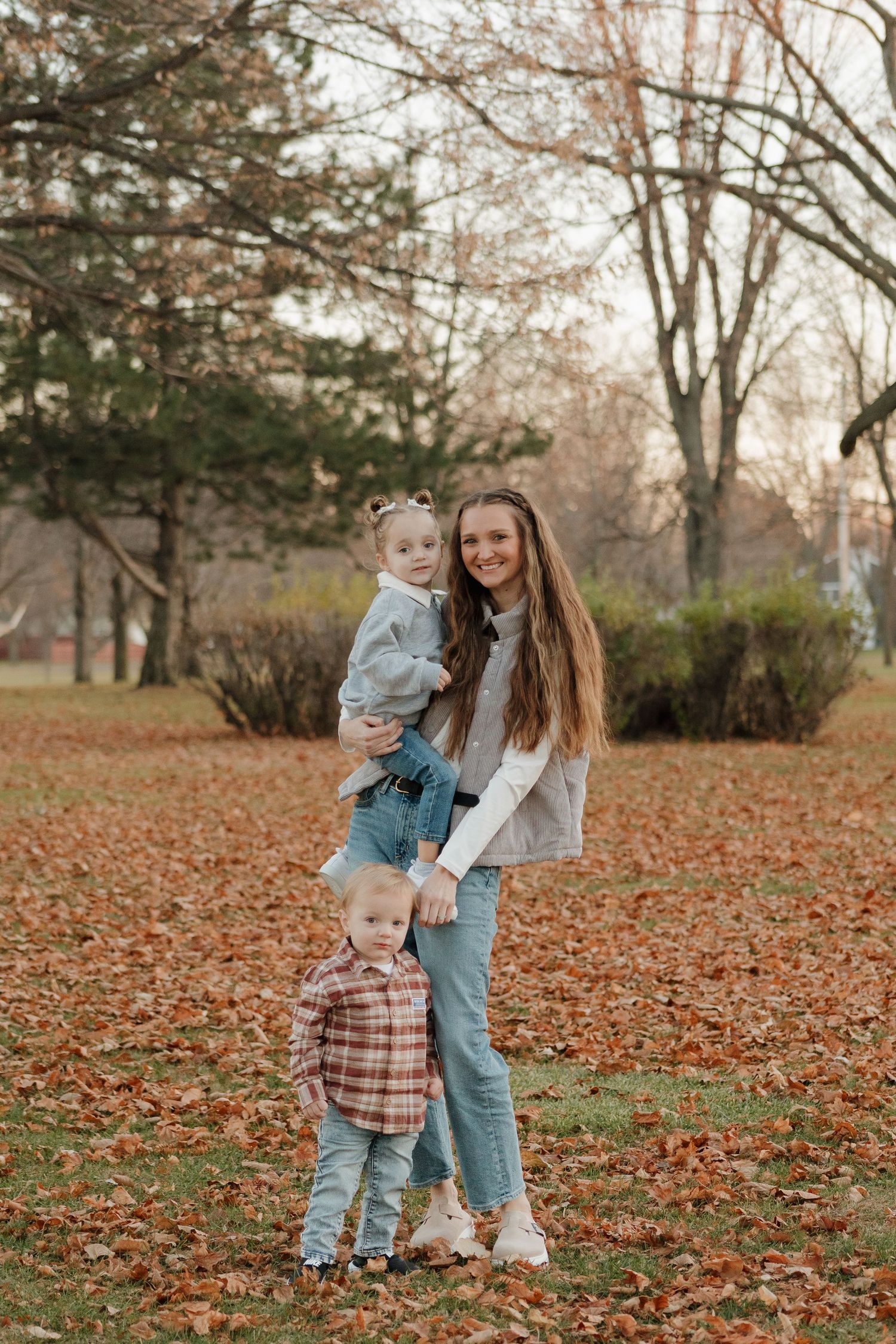 Candid moments of playtime in a park covered with fallen autumn leaves.