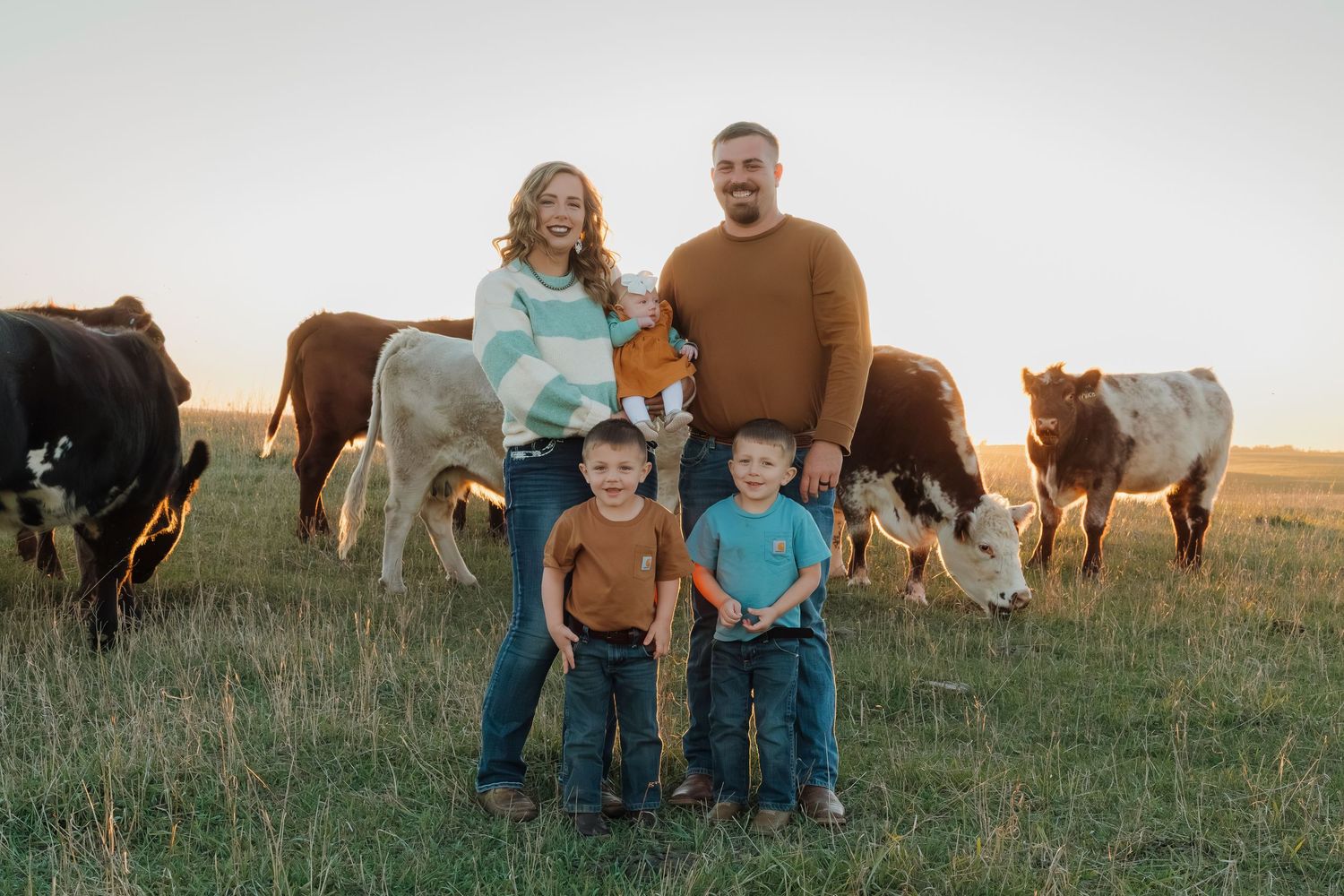 Family standing in a field at sunset with grazing horses in the background.