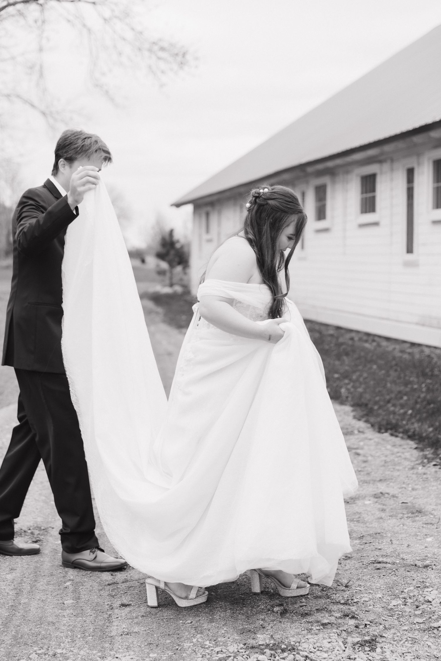Wedding couple walking together on dirt path with white buildings in background.