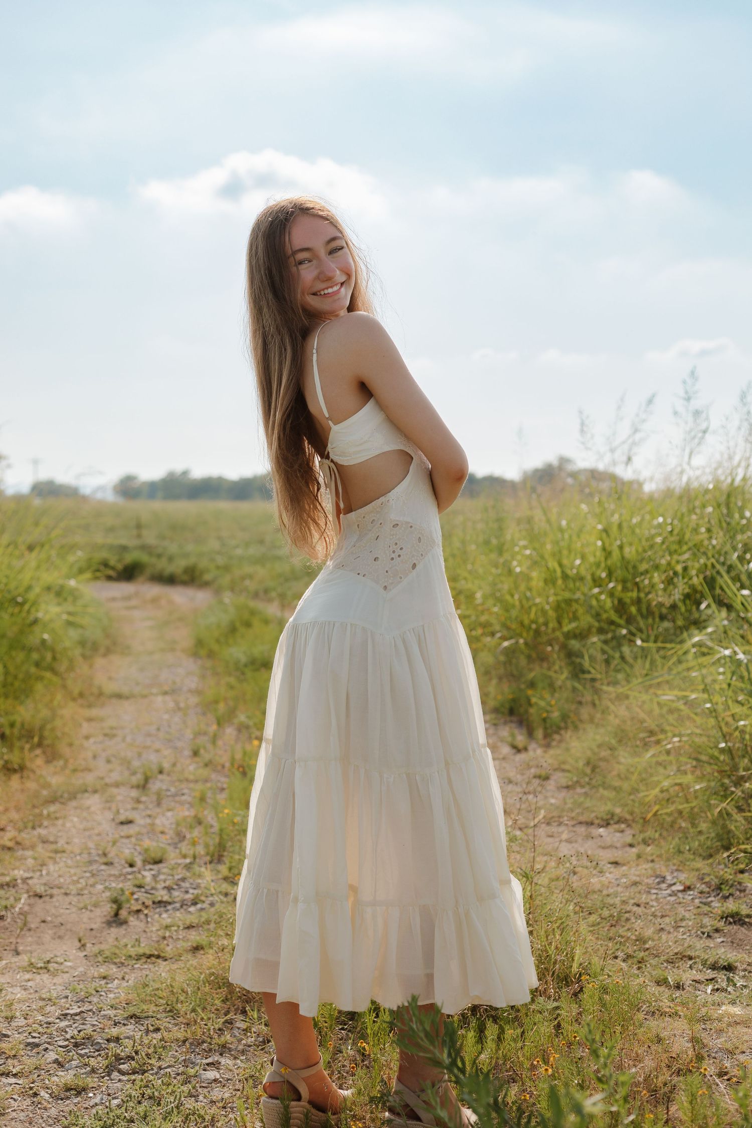 A flowing white summer dress photographed on a dirt path through a sunny meadow.