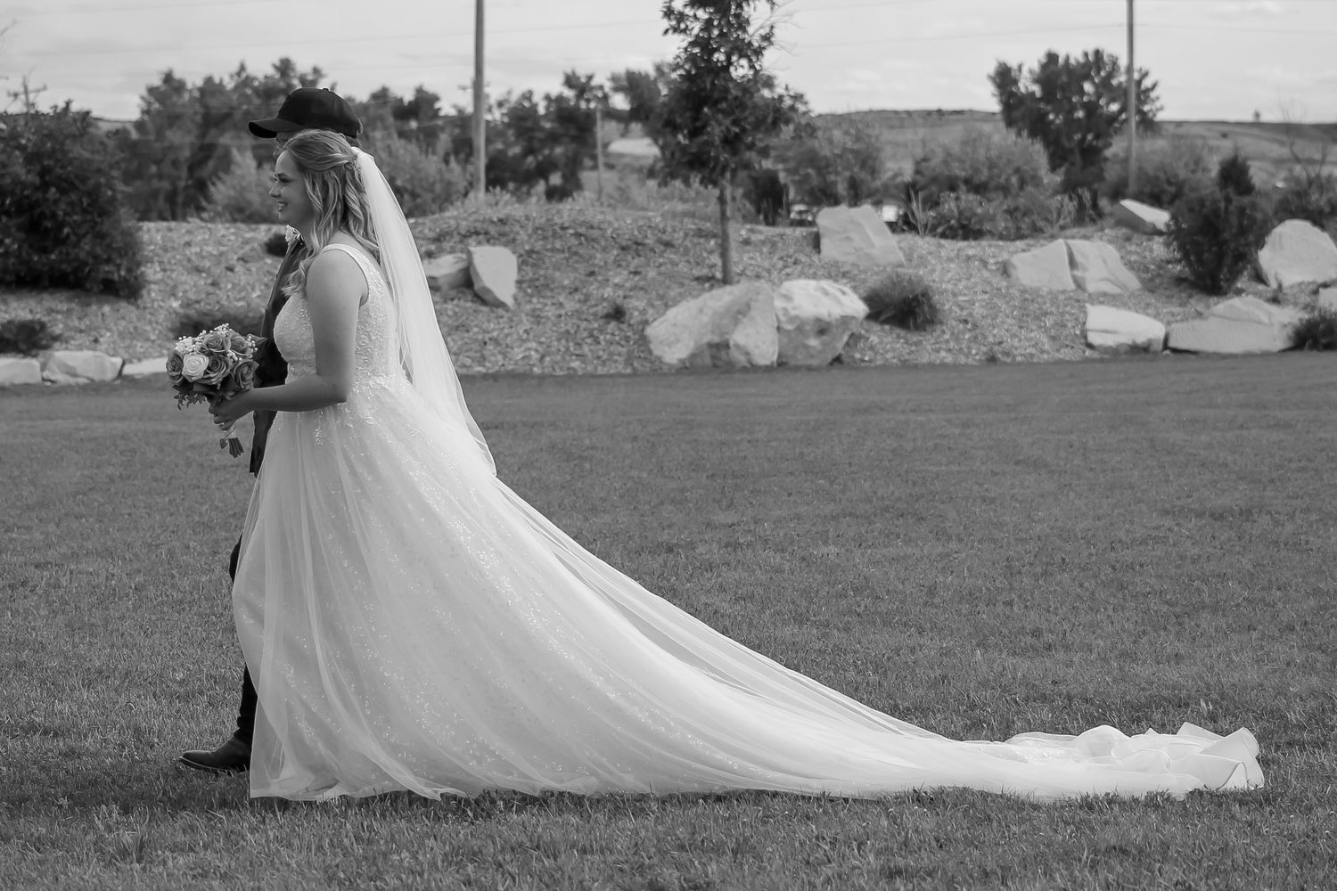 A flowing white wedding dress train spreads across a grassy field at Generations Wedding and Events in Rapid City, South Dakota.