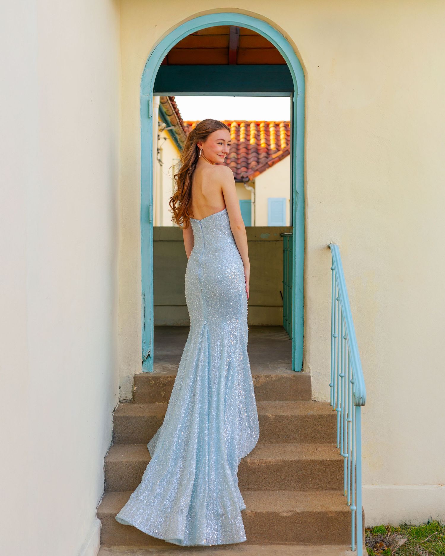 A flowing blue dress twirls in front of turquoise-trimmed archways and cream walls.