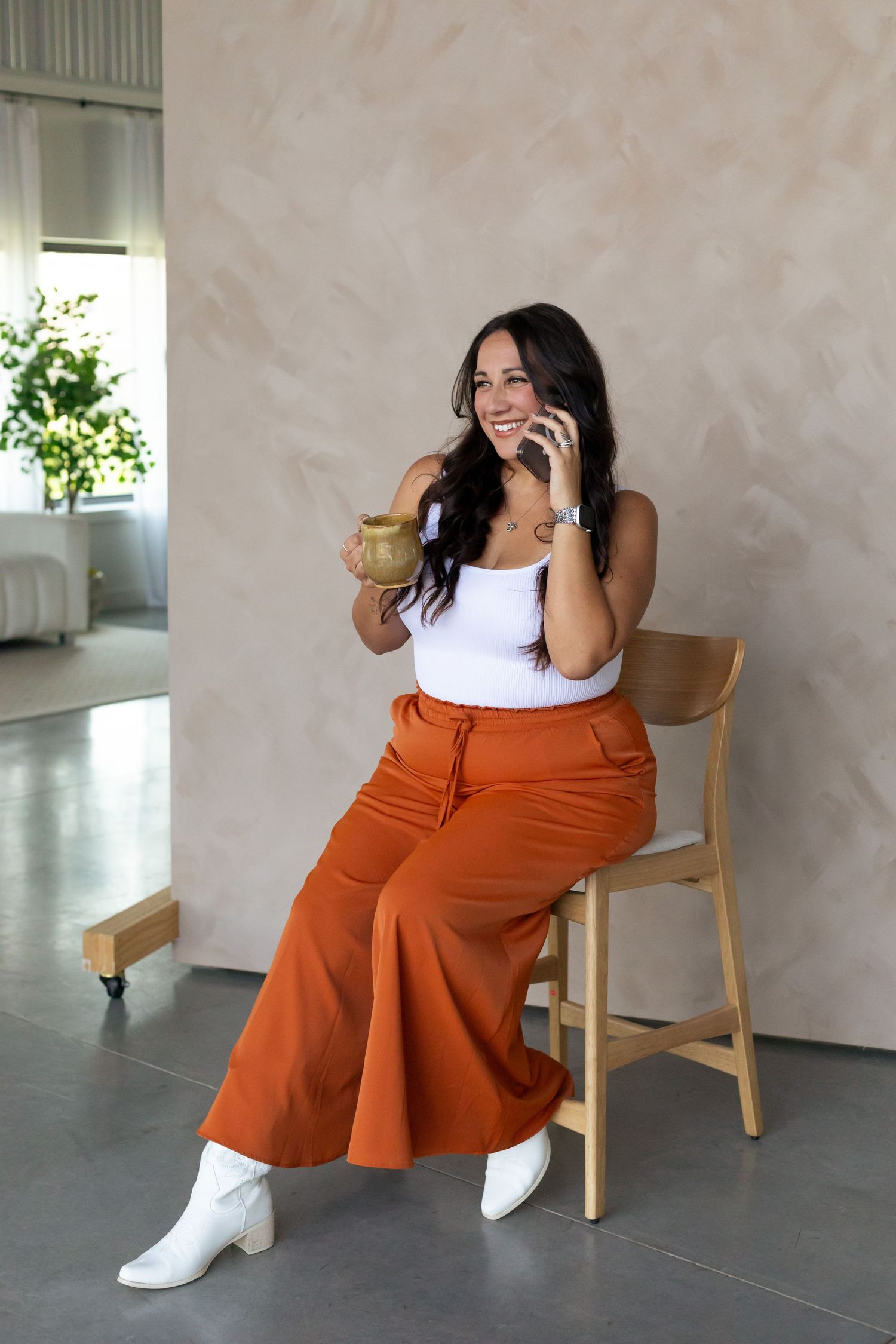 Fashion lifestyle photos of someone wearing orange wide-leg pants and white top while sitting in wooden chair.