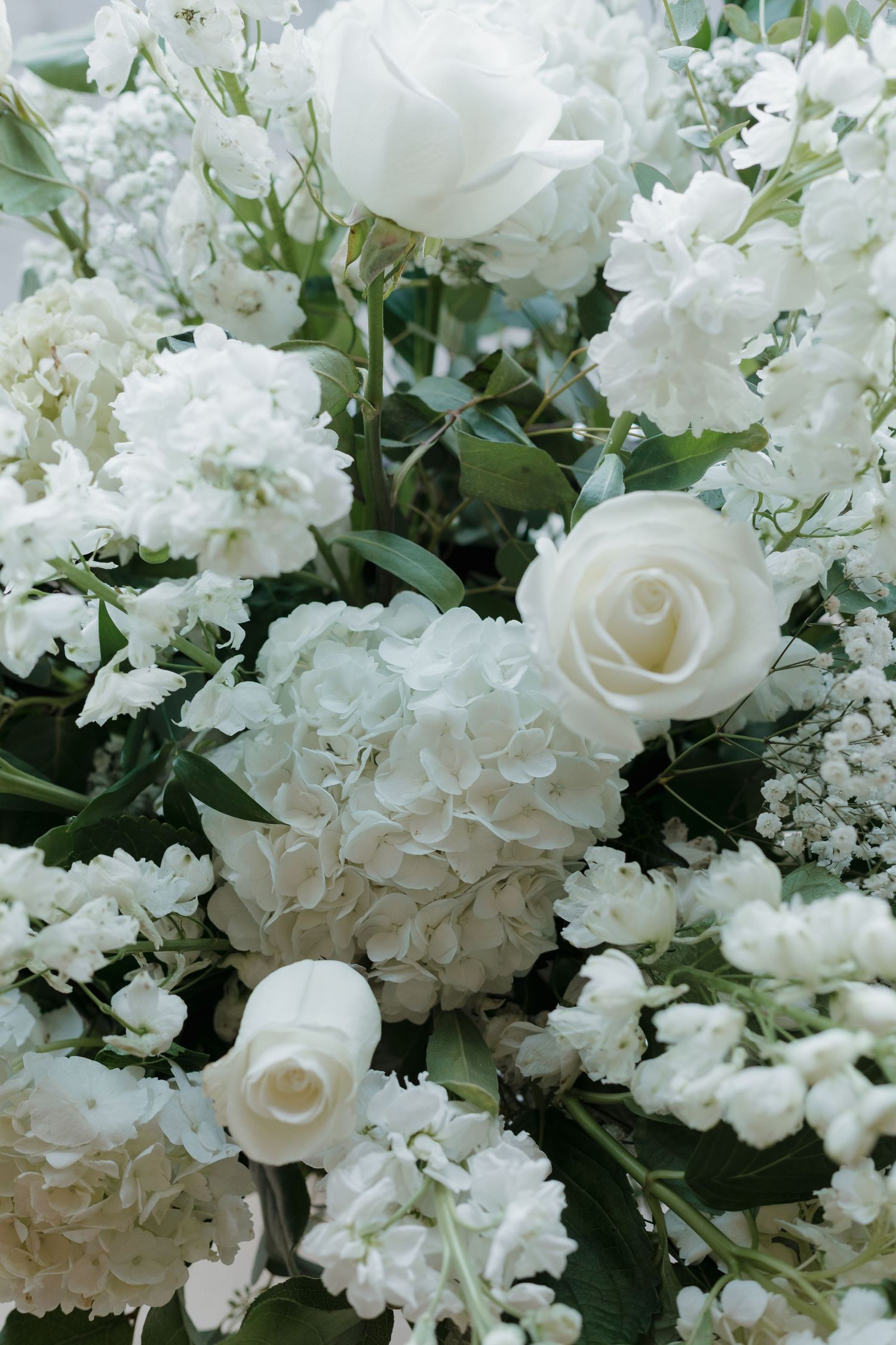 Elegant white floral arrangement featuring roses and hydrangeas with delicate greenery.