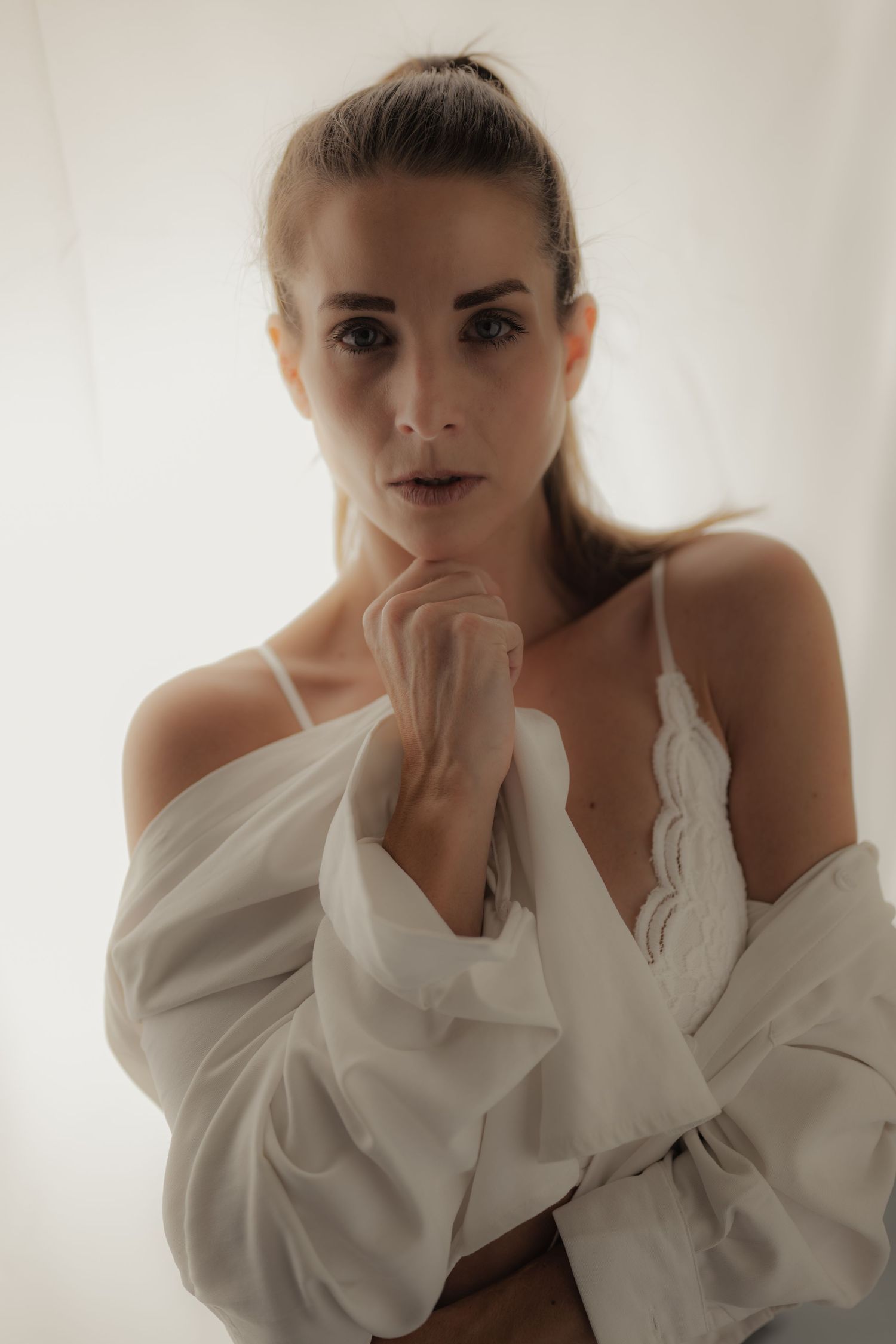 Woman in white off-shoulder blouse and lace camisole poses against bright white background.