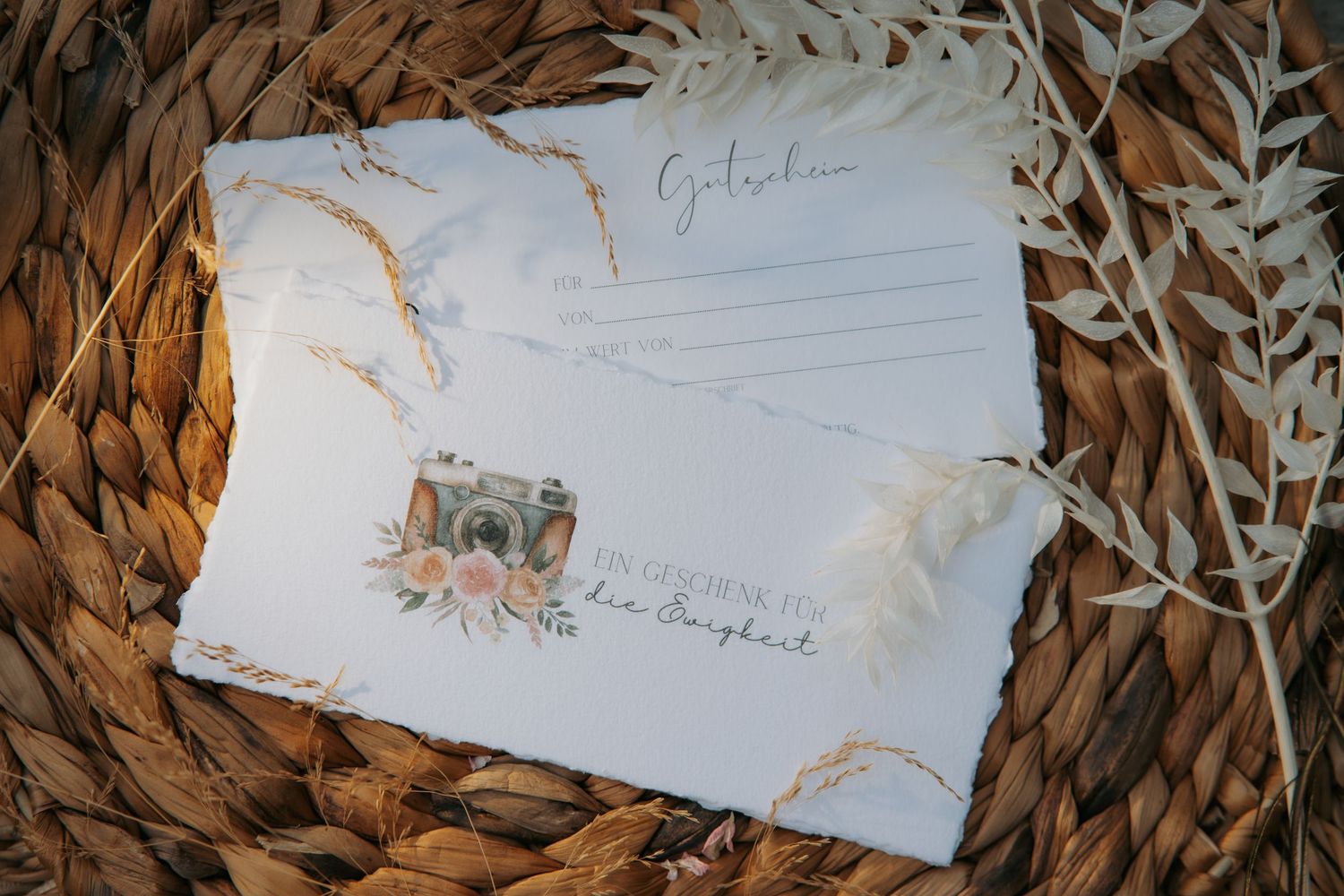 Elegant wedding stationery with floral camera design on woven backdrop with dried botanicals.