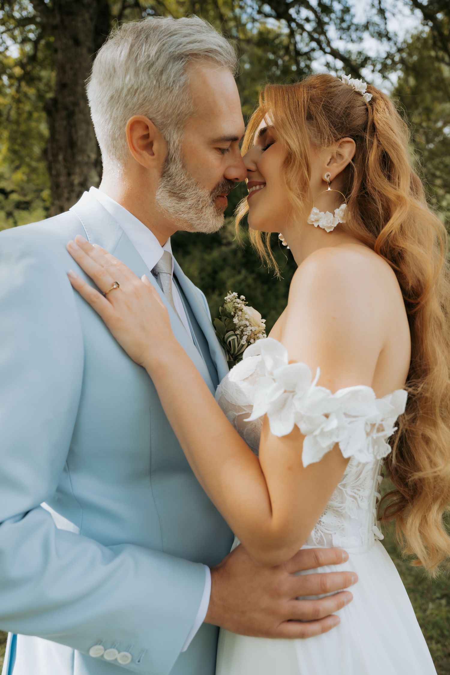 A bride and groom share a romantic moment outdoors, nearly kissing, dressed in wedding attire.