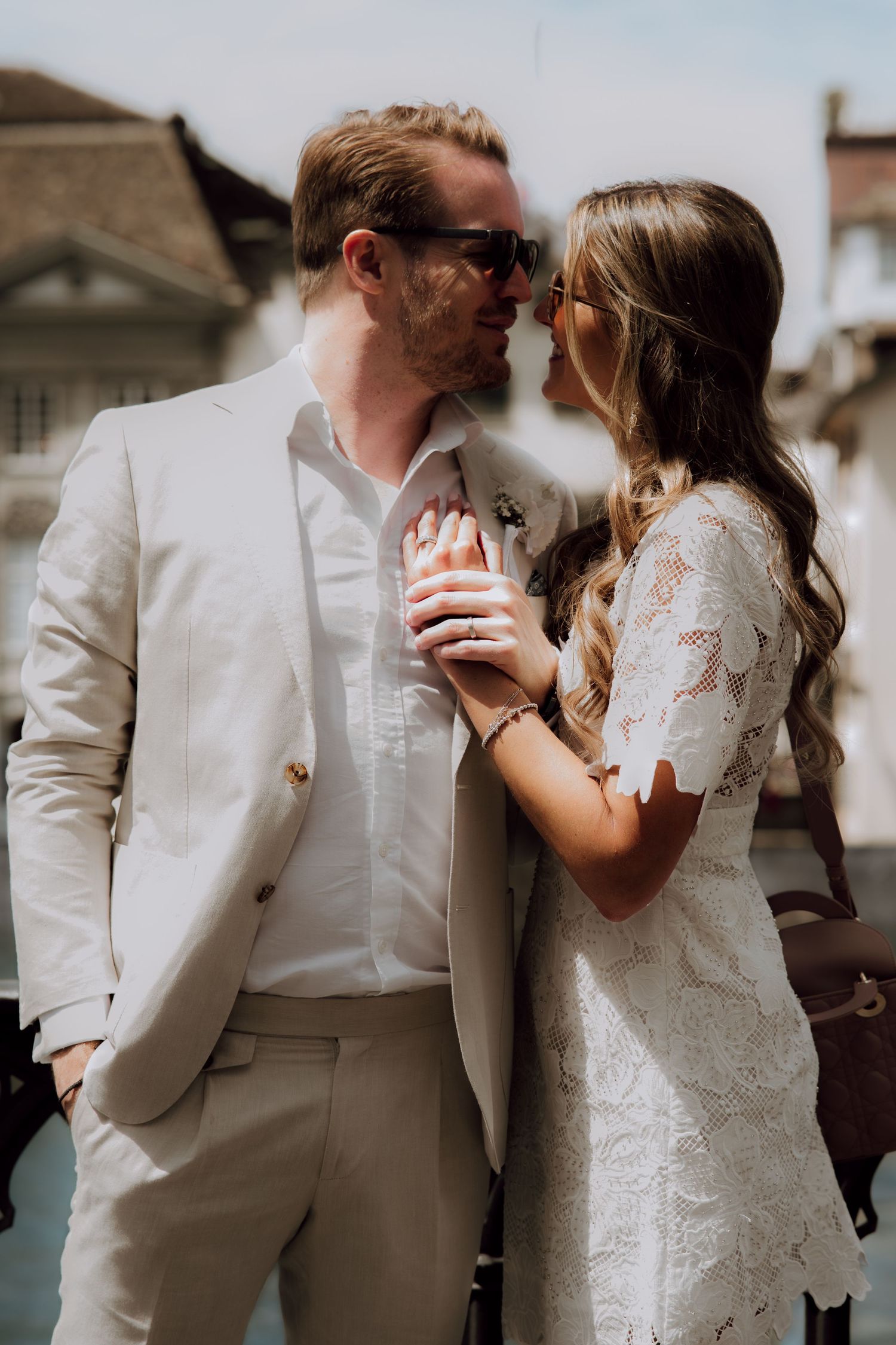 Couple in wedding attire sharing a romantic moment outdoors, groom in beige suit, bride in white lace dress.