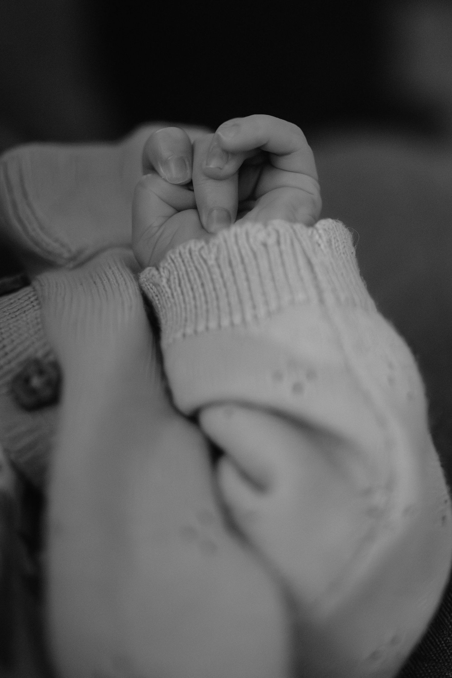 Black and white close-up of a baby's tiny hand grasping a knitted white sock, capturing delicate newborn details.
