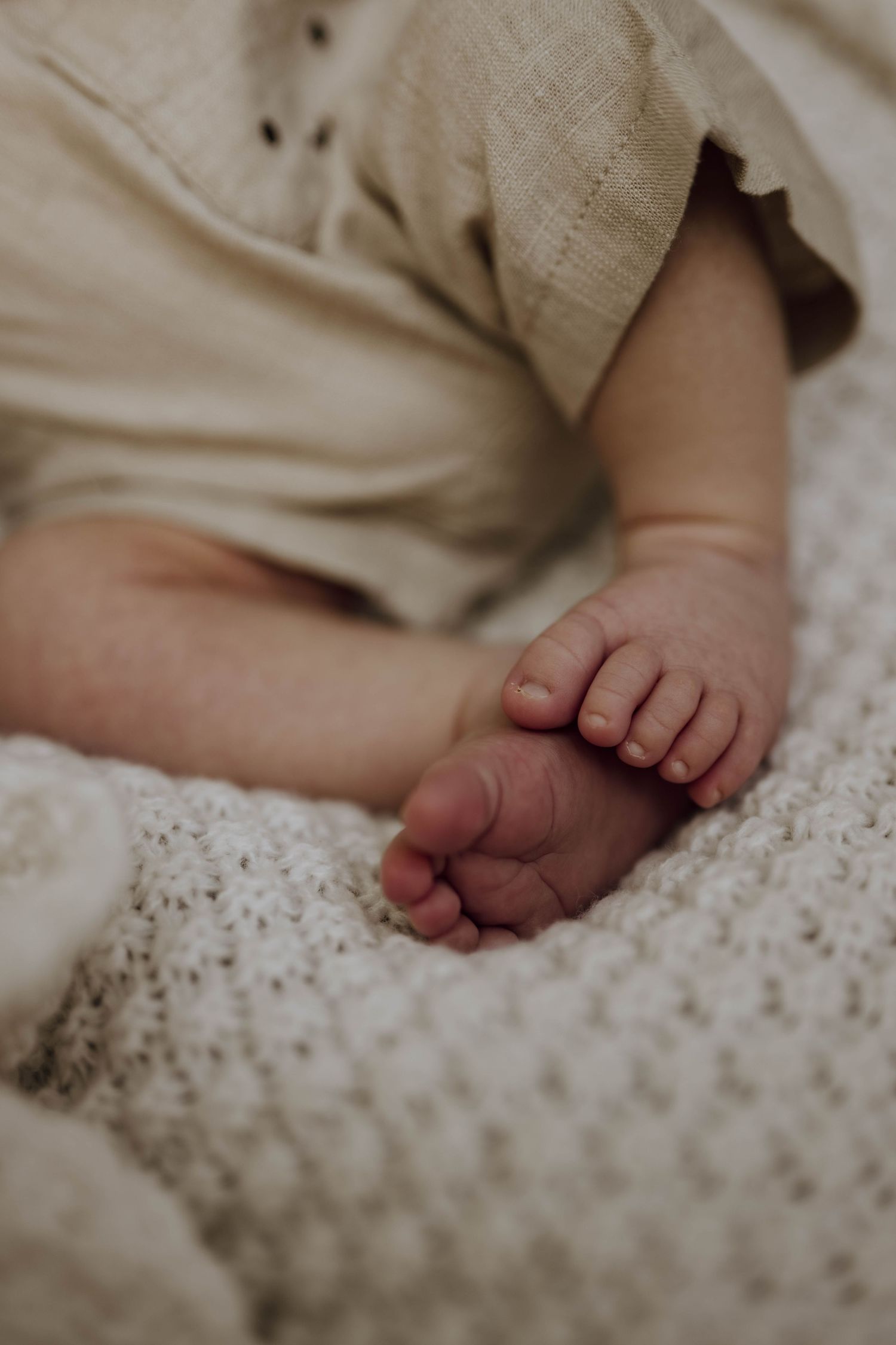 Close-up of tiny newborn baby feet and toes resting on a soft white knit blanket.