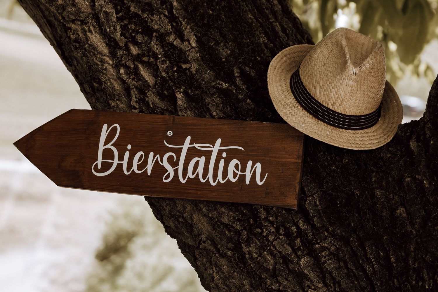 Wooden arrow sign reading Bierstation mounted on a tree trunk with a straw hat, pointing to a beer station.