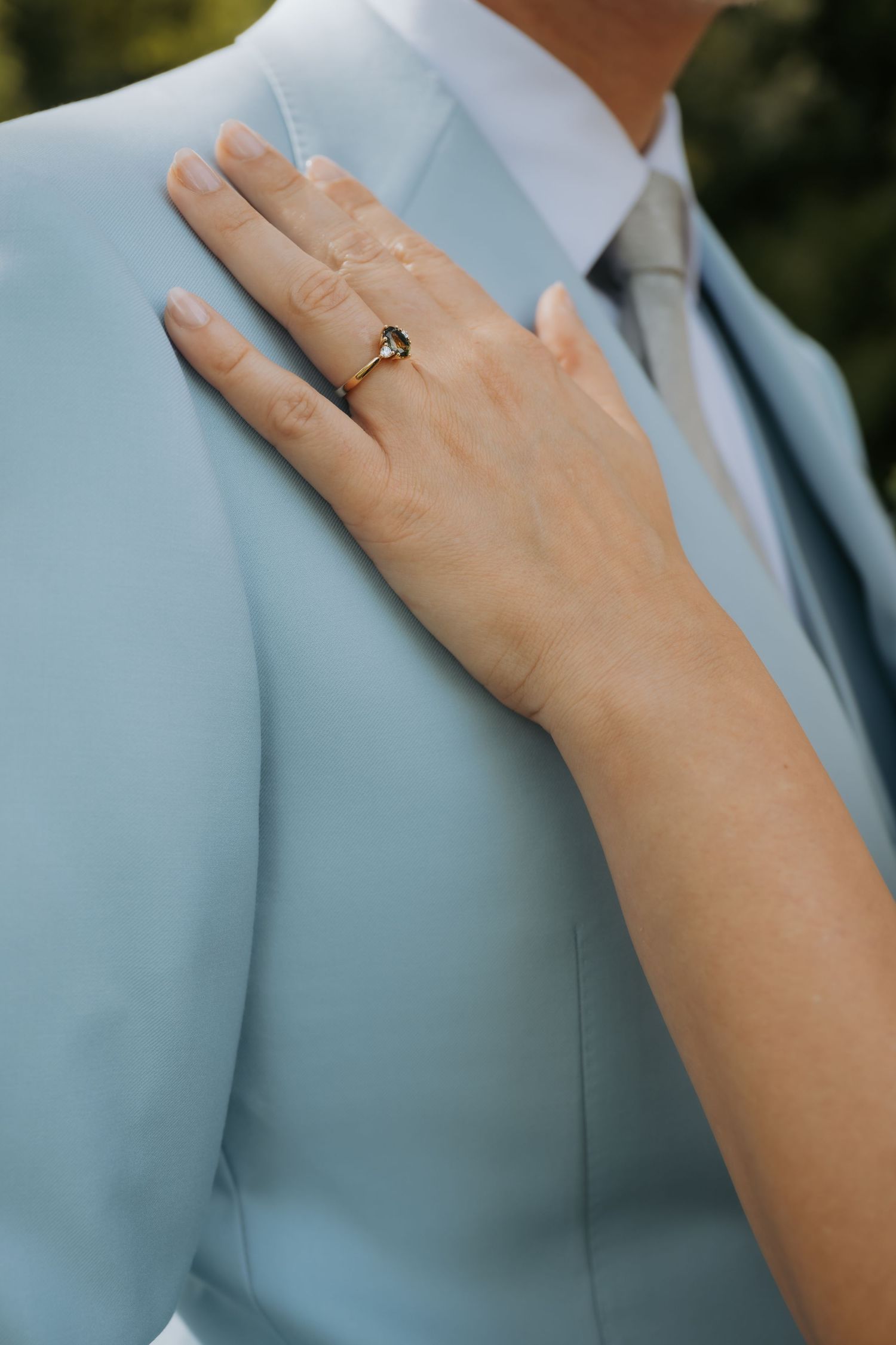 Close-up of a bride's hand with a gold diamond ring resting on a groom's light blue suit jacket.
