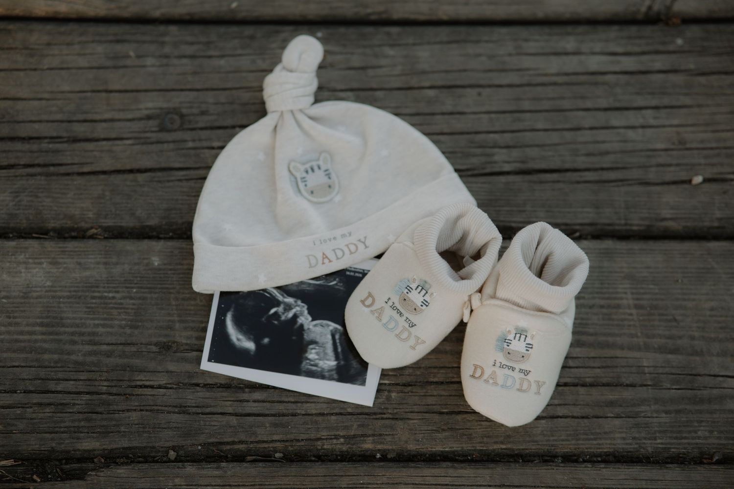 Baby hat, booties, and ultrasound photo on wood, with 'I Love You Daddy' embroidery, perfect newborn gift set.