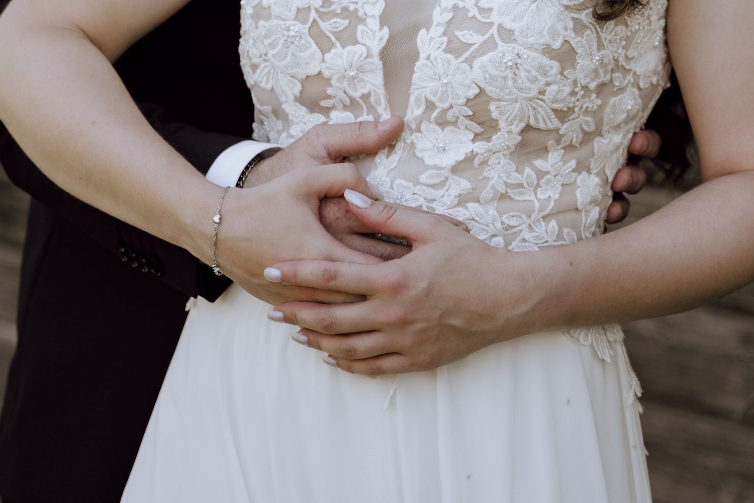 Bride and groom holding hands at wedding, close-up of white lace bridal gown and groom suit.