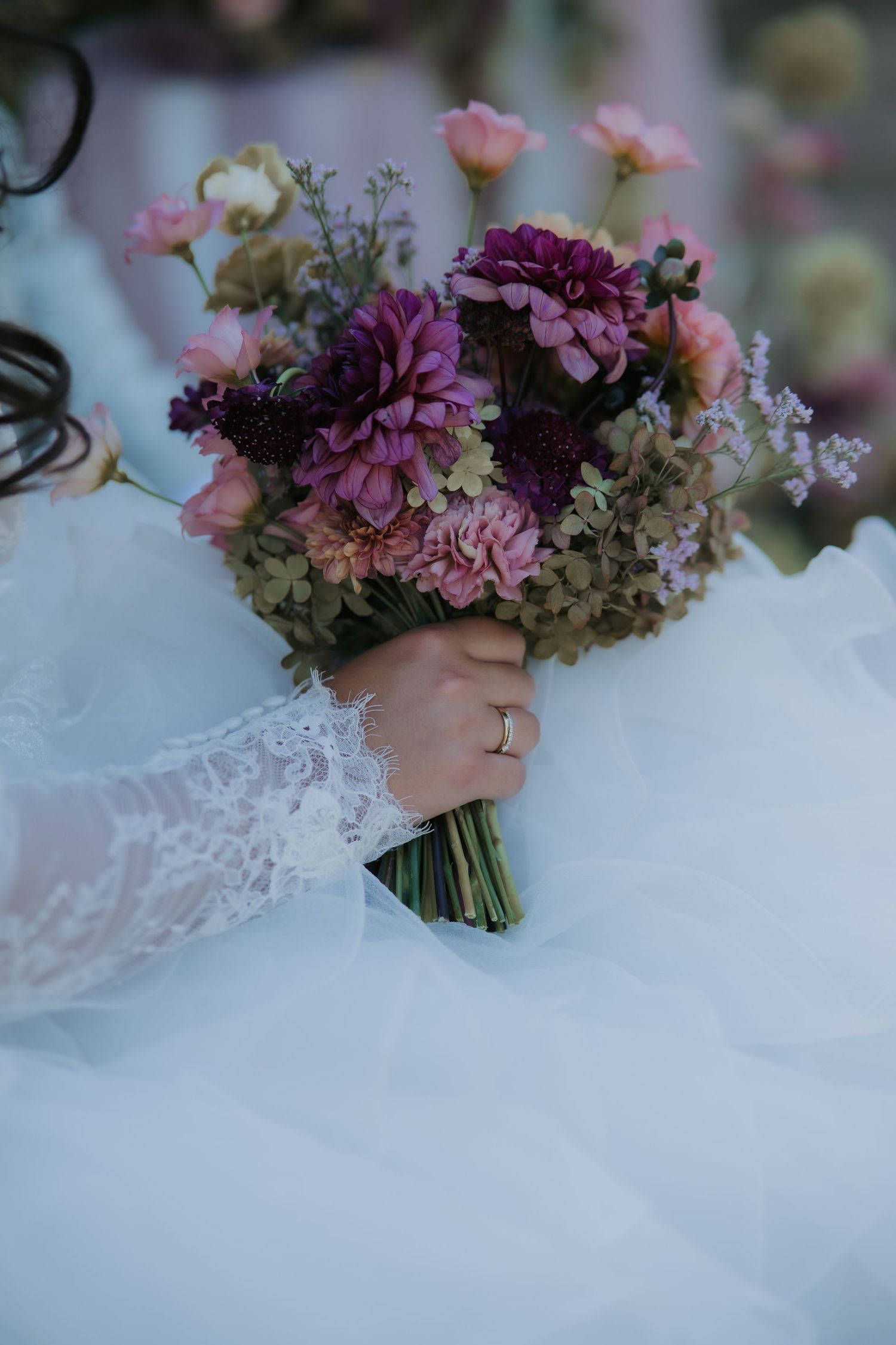 Bride in lace wedding dress holding a purple and pink bridal bouquet with dahlias and hydrangeas.
