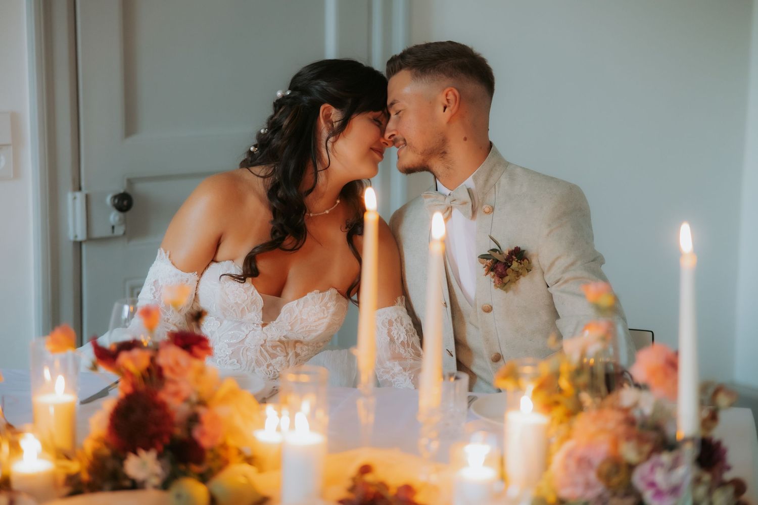 Bride and groom share a romantic moment at candlelit reception table adorned with colorful floral arrangements.