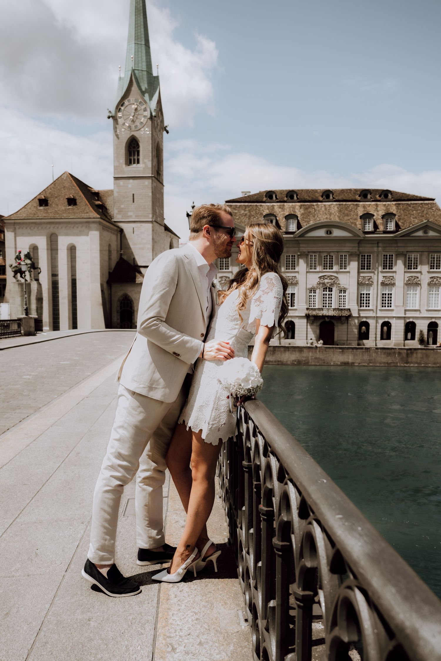 Couple sharing a romantic kiss on a bridge in Zurich, Switzerland, with Fraumunster Church in the background.
